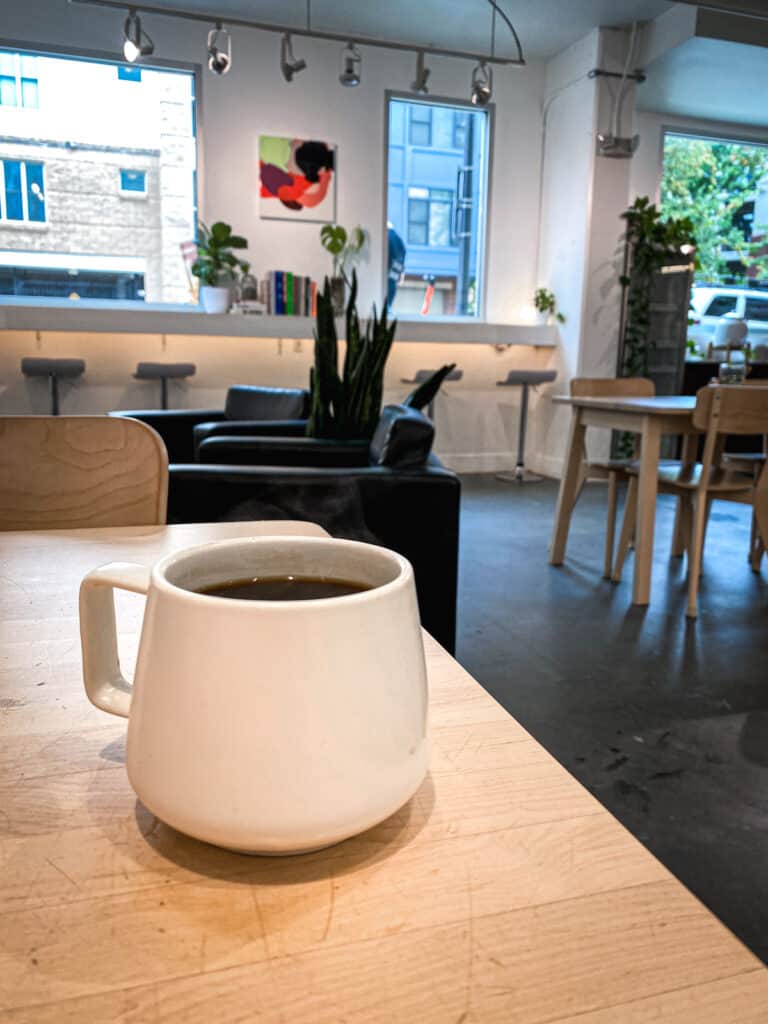 A white mug on a table in an empty coffee shop with white walls