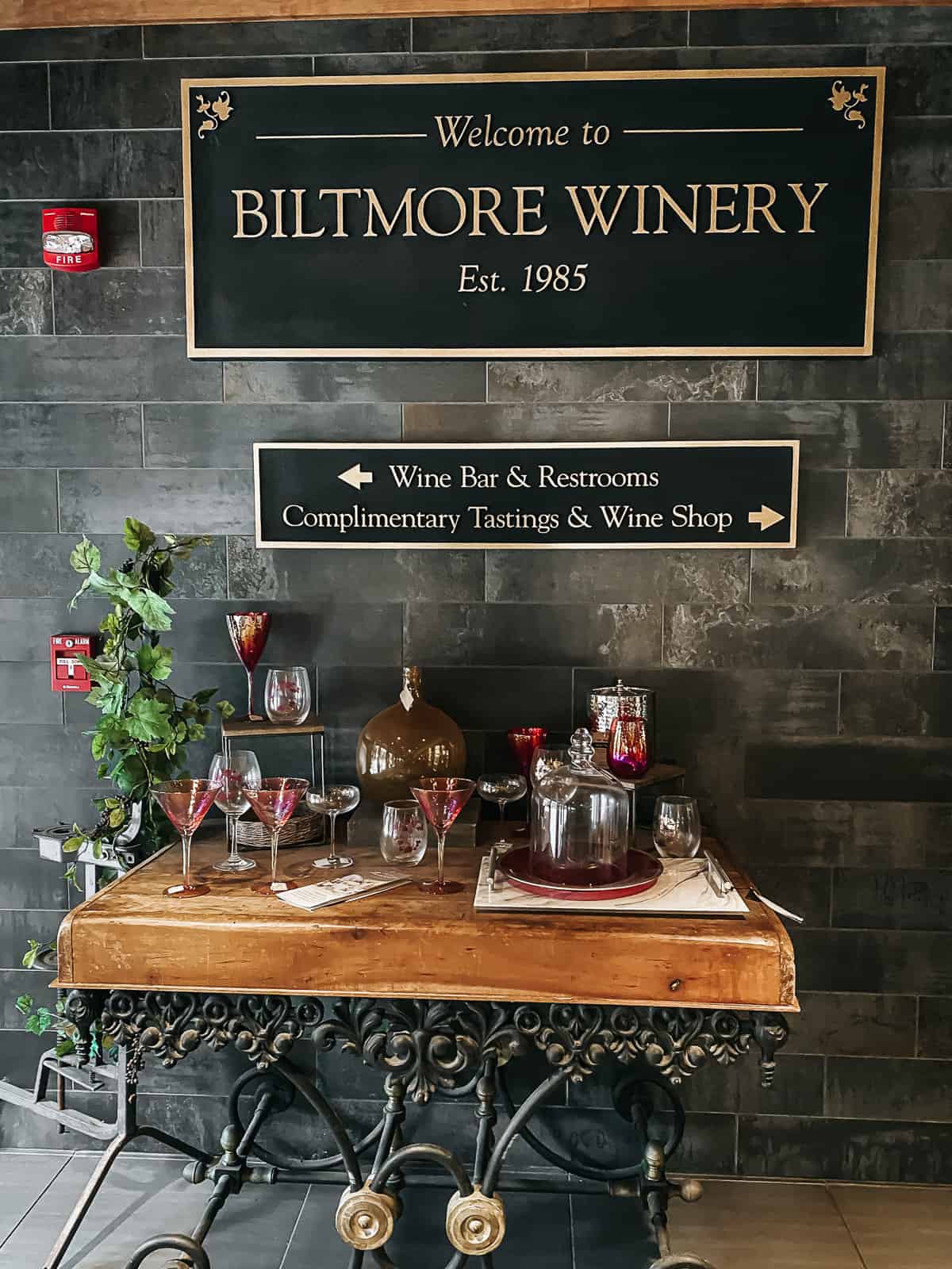 A black sign on a wall for the Biltmore Winery with martini glasses on a table below it