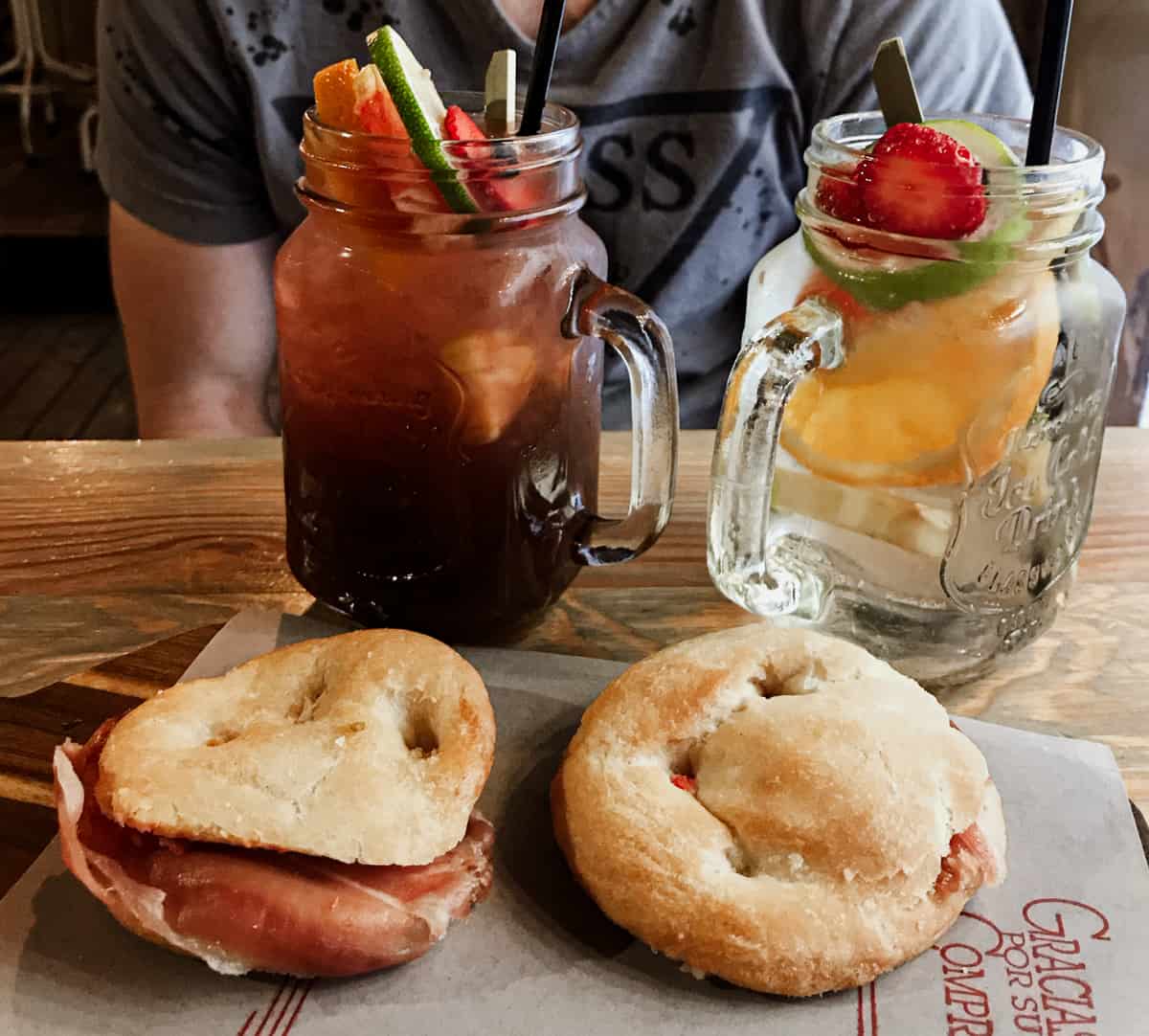 2 jars of sangria on a table with two small sandwiches with ham on them