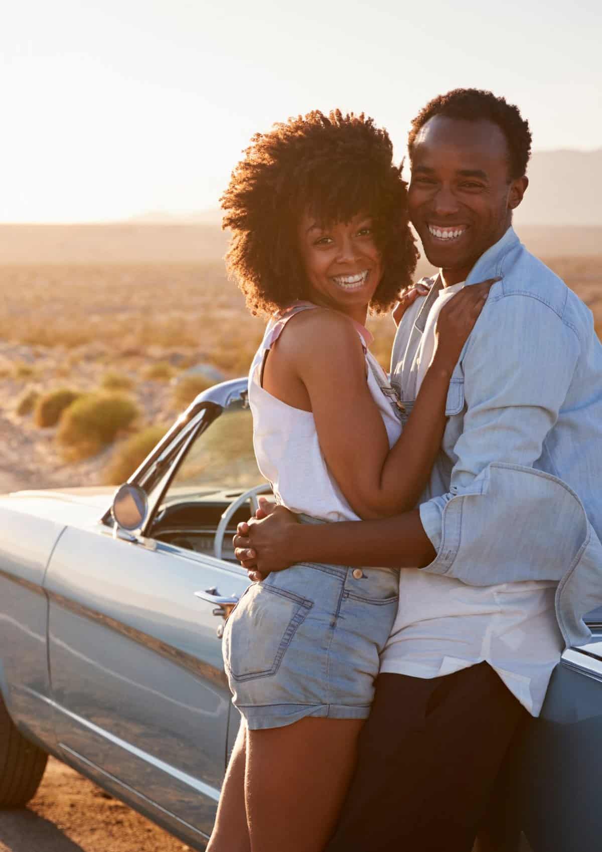 A couple standing outside of a blue convertible in the desert. 