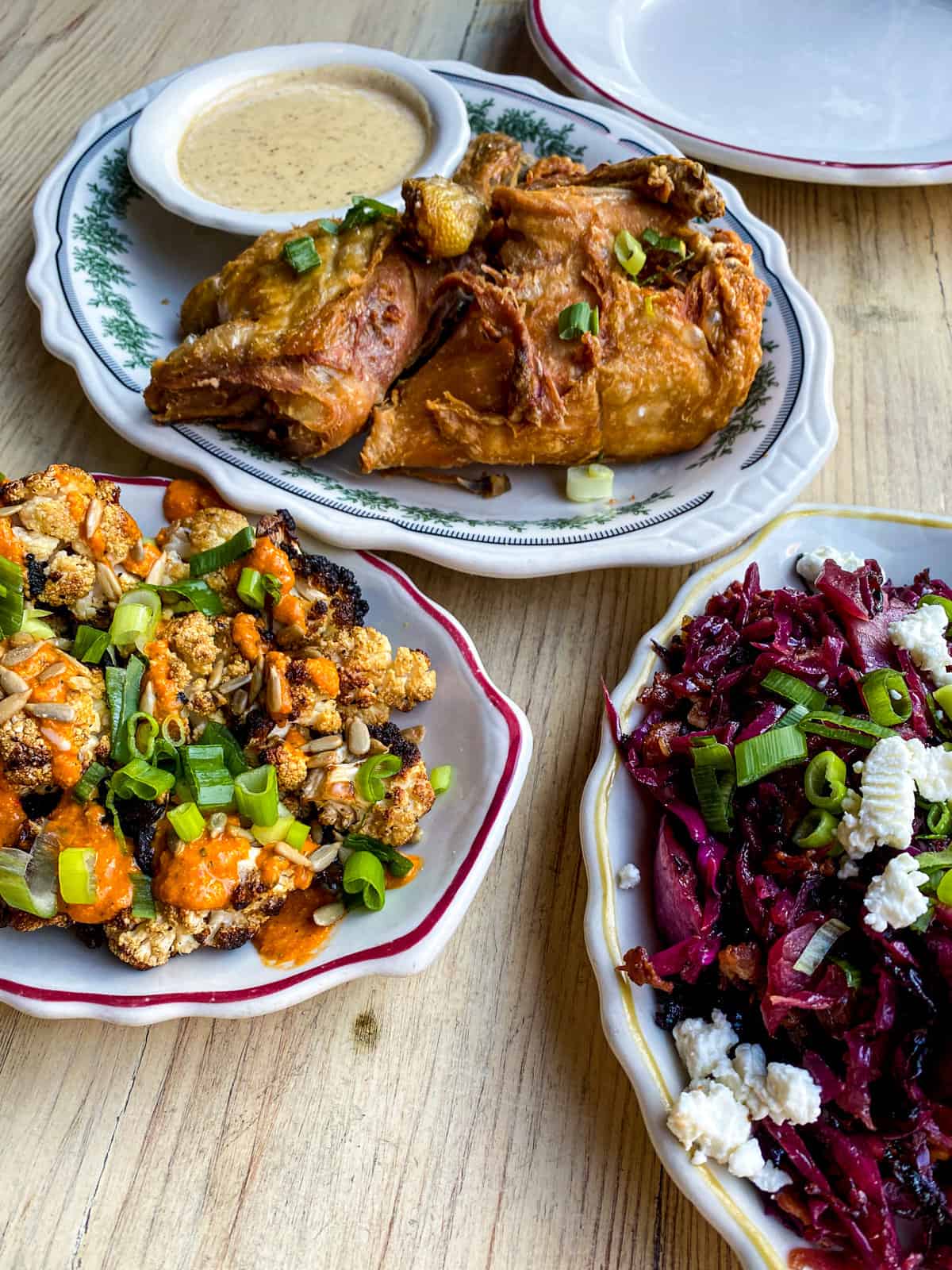 3 plates on a table at Haberdish restaurant. One has fried chicken, one has roasted cauliflower and one has purple cabbage