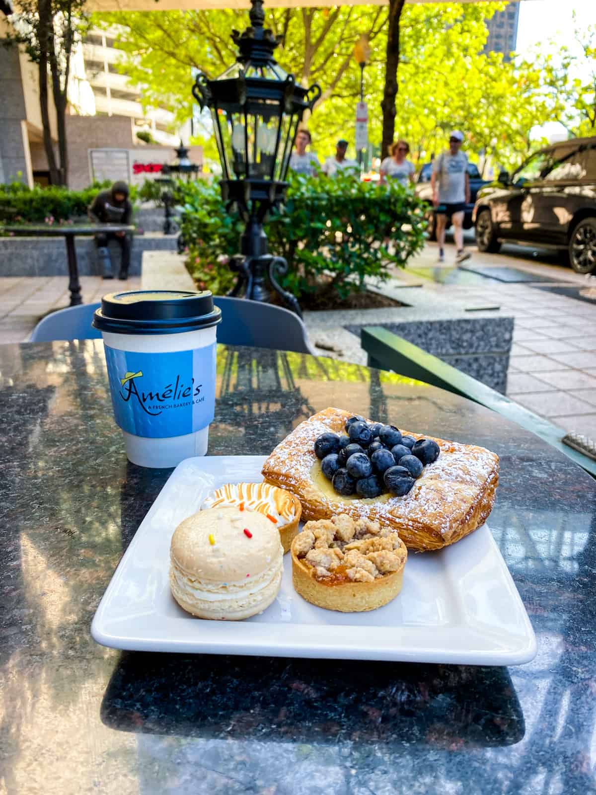 4 pastries on a white plate sitting on a table with a to-go cup that says Amelies on it.