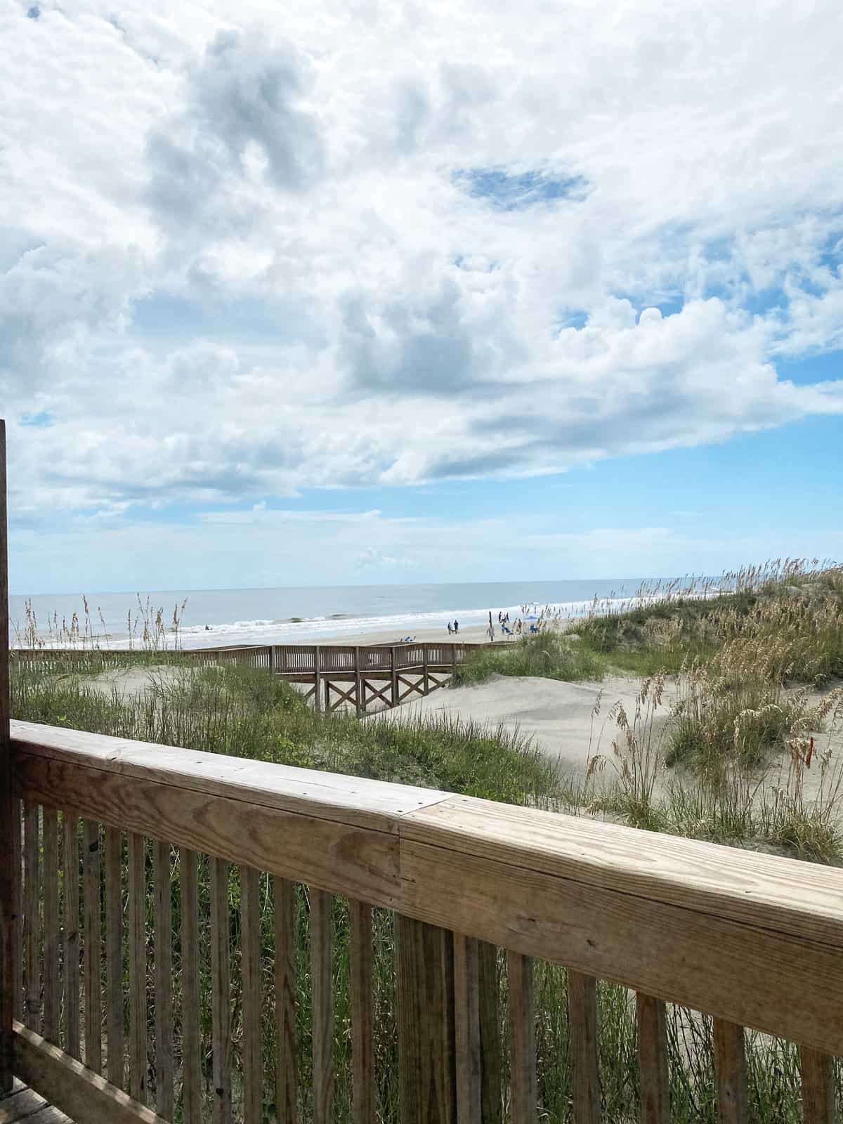 a wooden railing on a boardwalk on a beach with a blue, cloudy sky