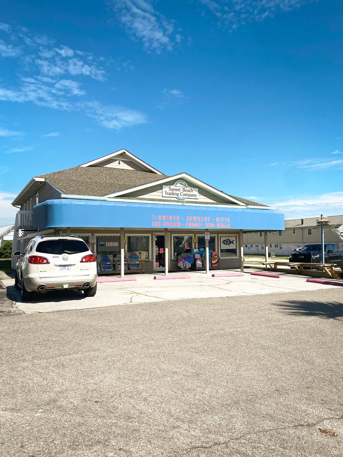 A blue building with a bright blue sky and  a car in front. The Sunset Beach Trading Company