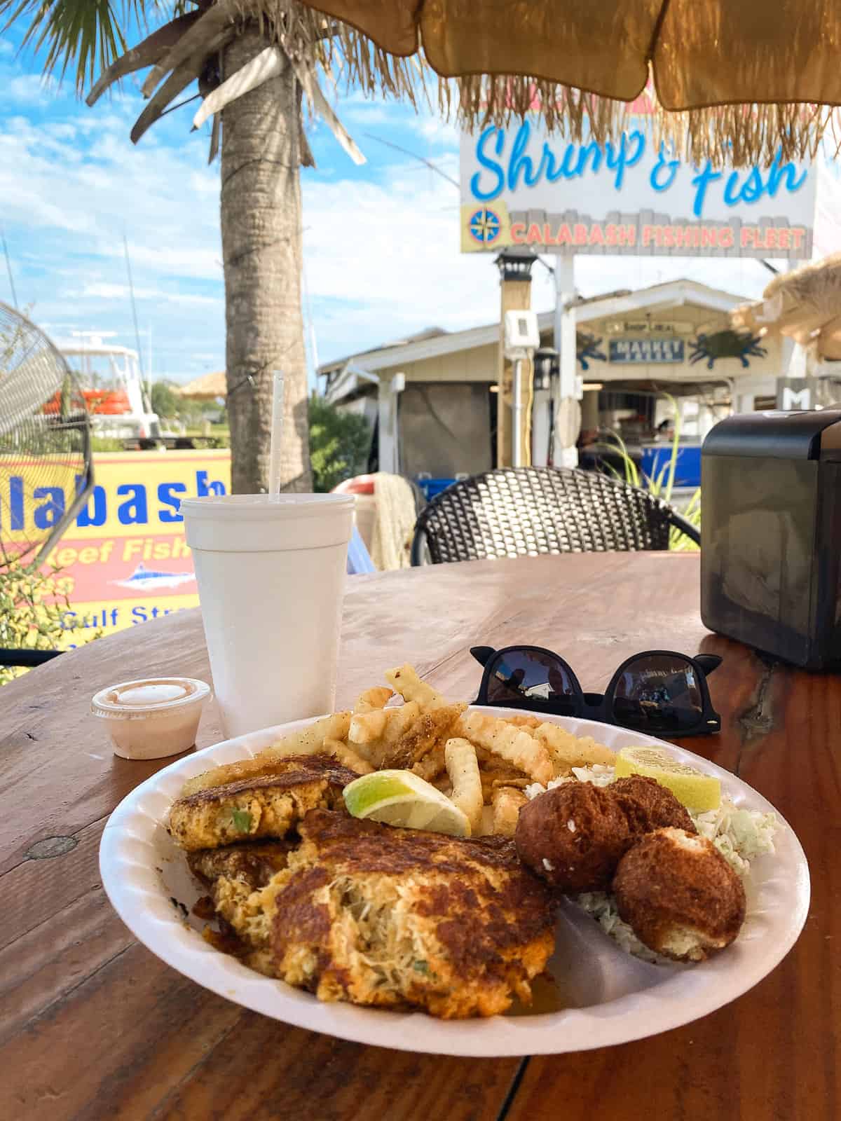 A photo of crab cakes on a paper plate at a casual outdoor seafood restaurant with palm umbrellas.