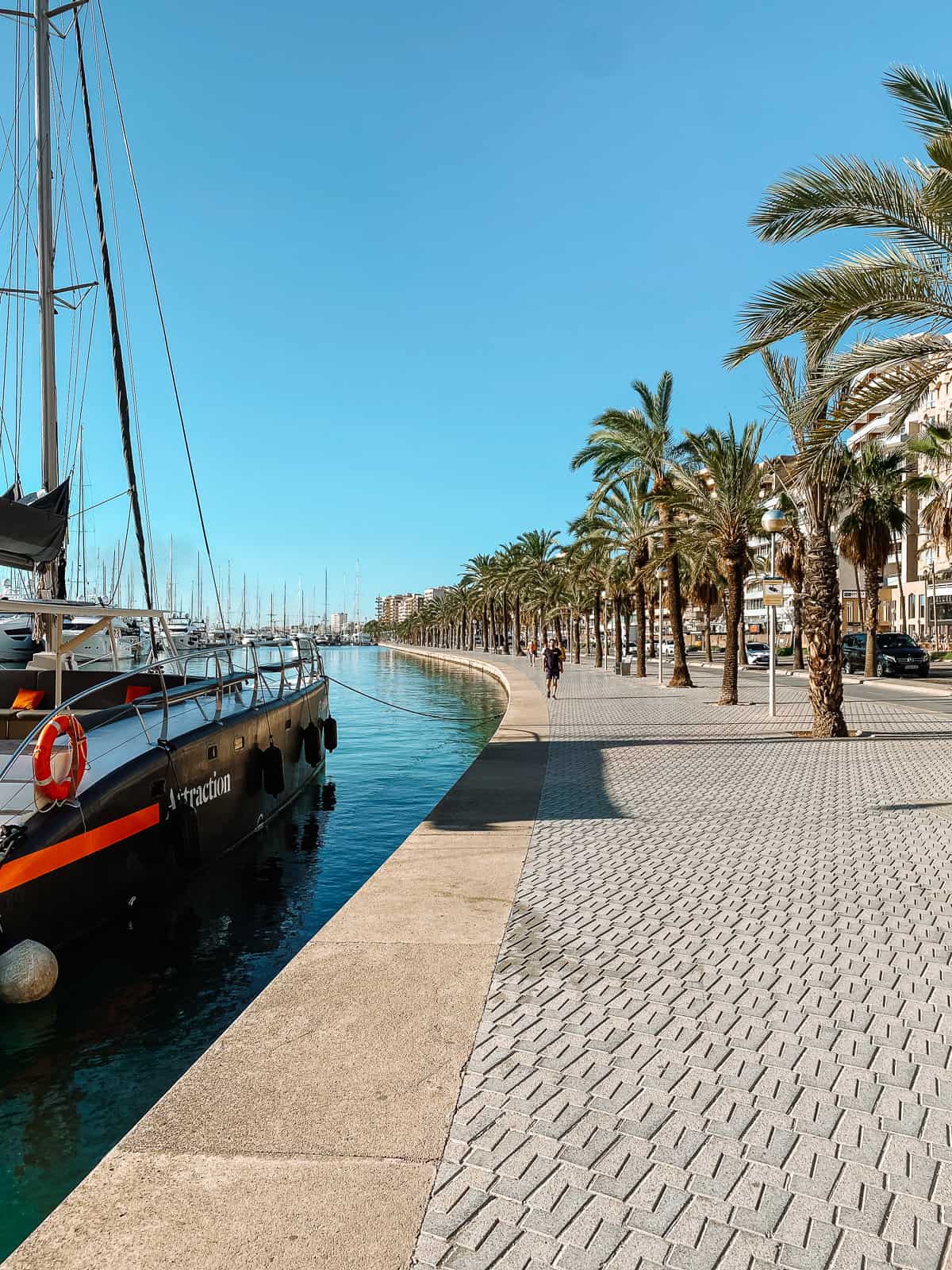 a stone walkway on the side of a harbor with a yacht