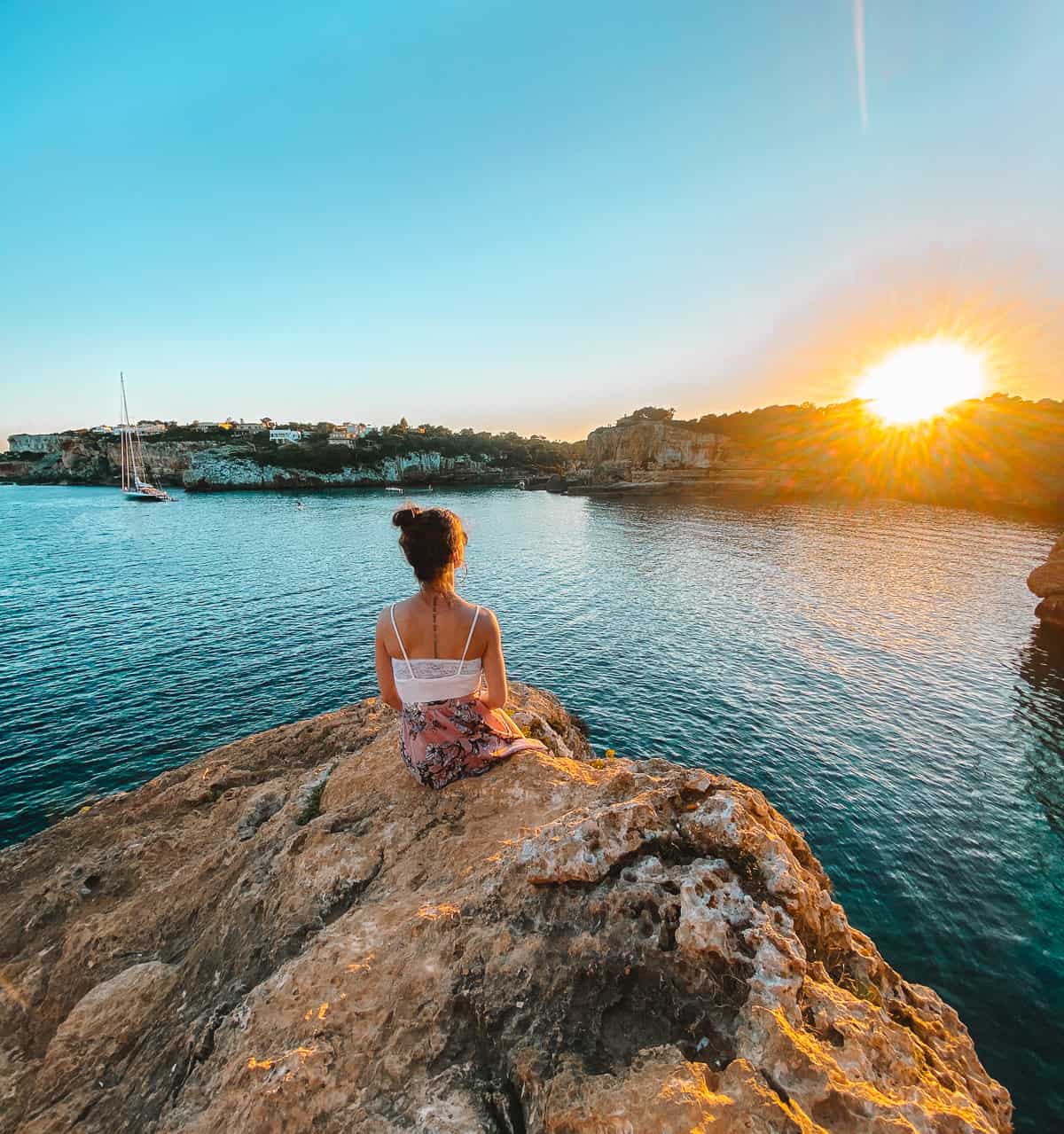 A woman sitting on a rock formation looking over the sunset on the ocean