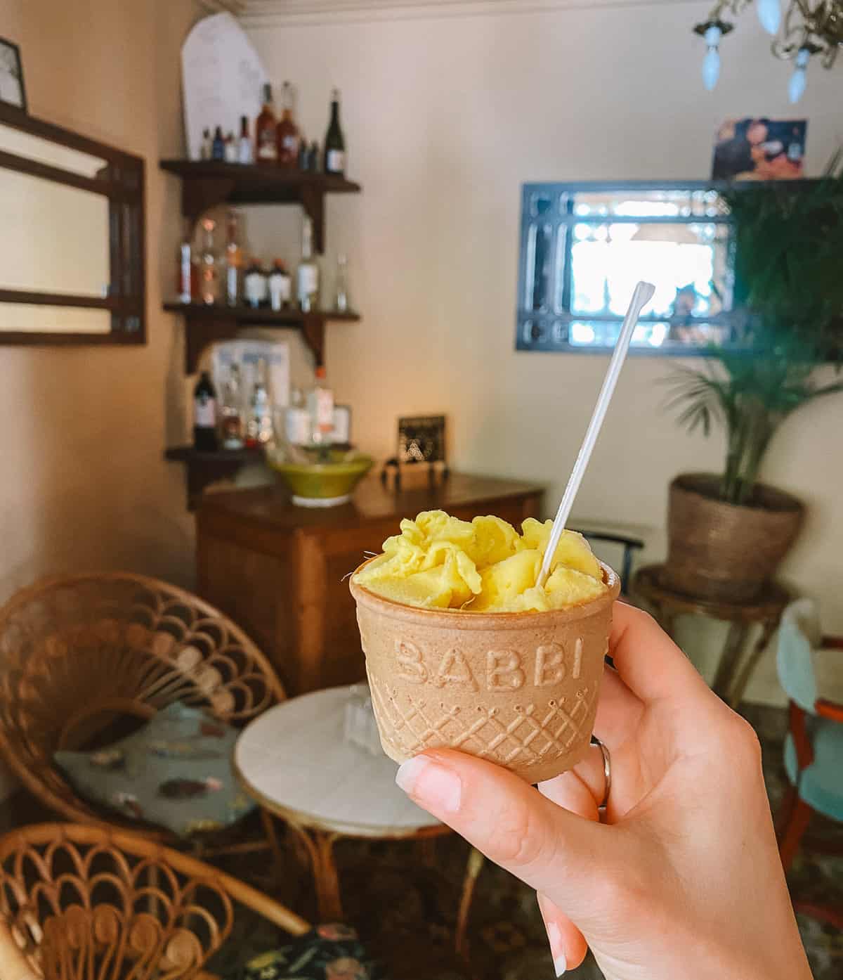 A hand holding a cup with mango sorbet in it