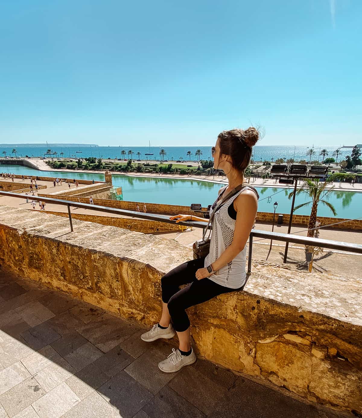a woman sitting on a stone barrier looking over the ocean