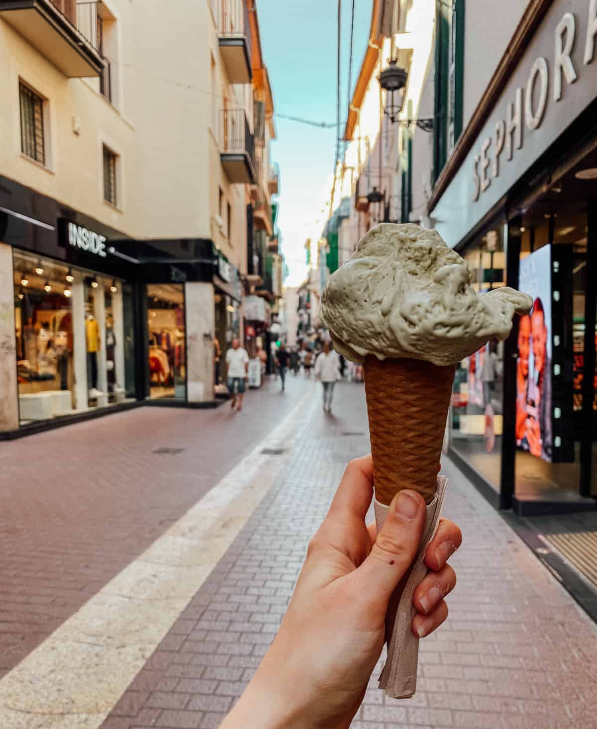 a hand holding a cone of green gelato on a busy street.