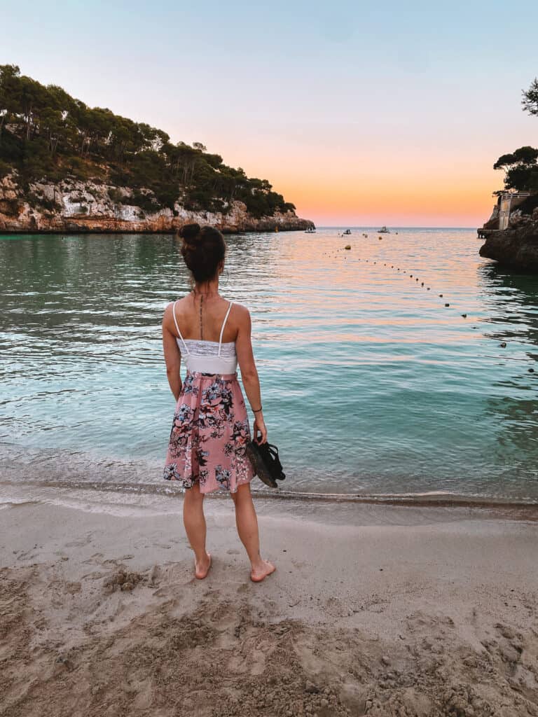 a girl standing on a beach in a pink dress with a sunset