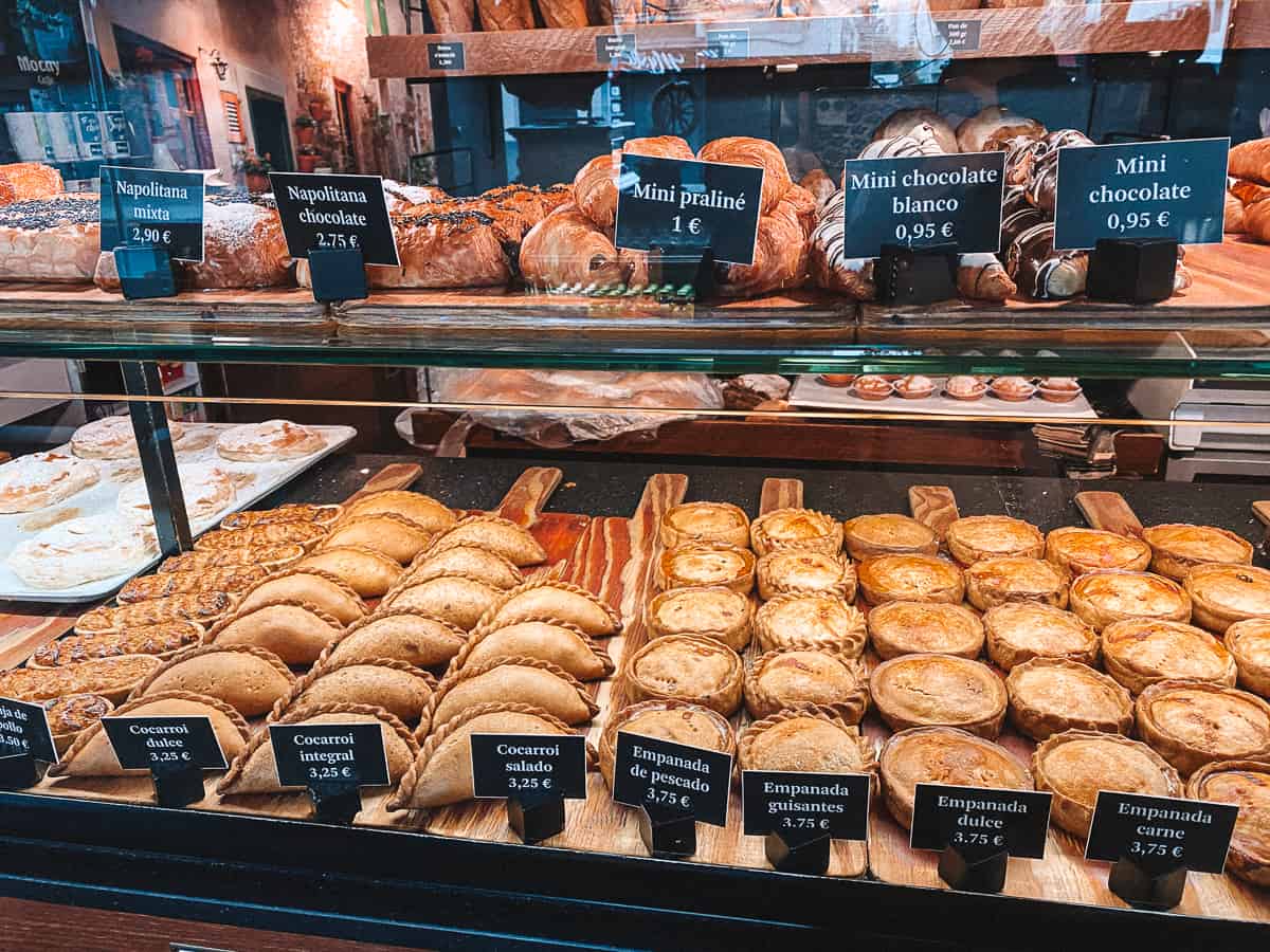 a bakery window filled with cocarroi and spanish panades