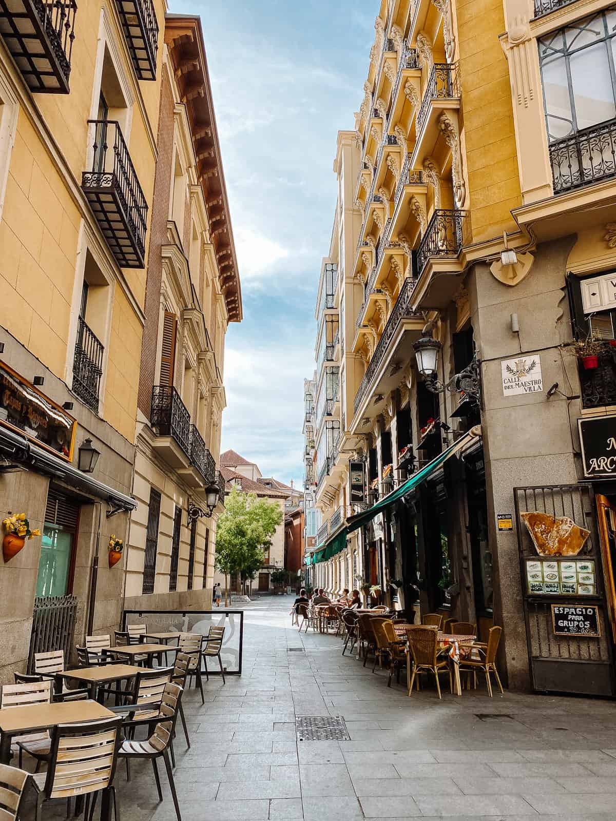 a beautiful side street with yellow buildings and cafe chairs in Madrid