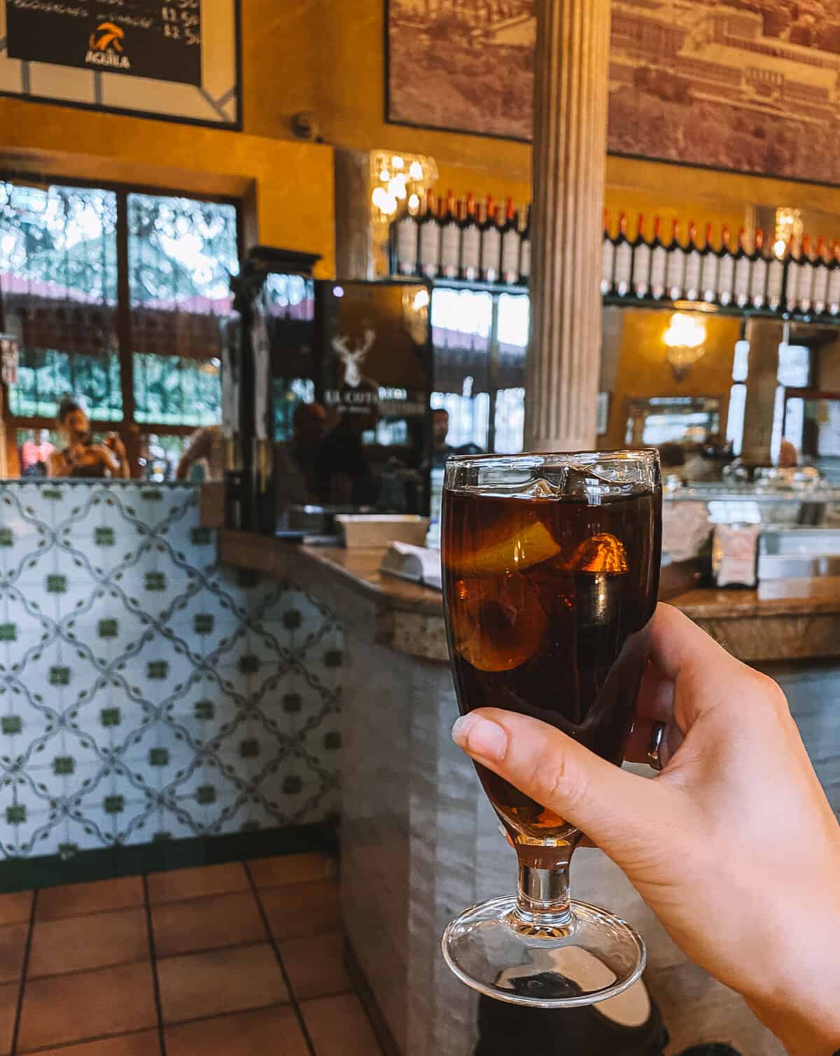 a hand holding a glass of vermouth in a tapas bar in Madrid