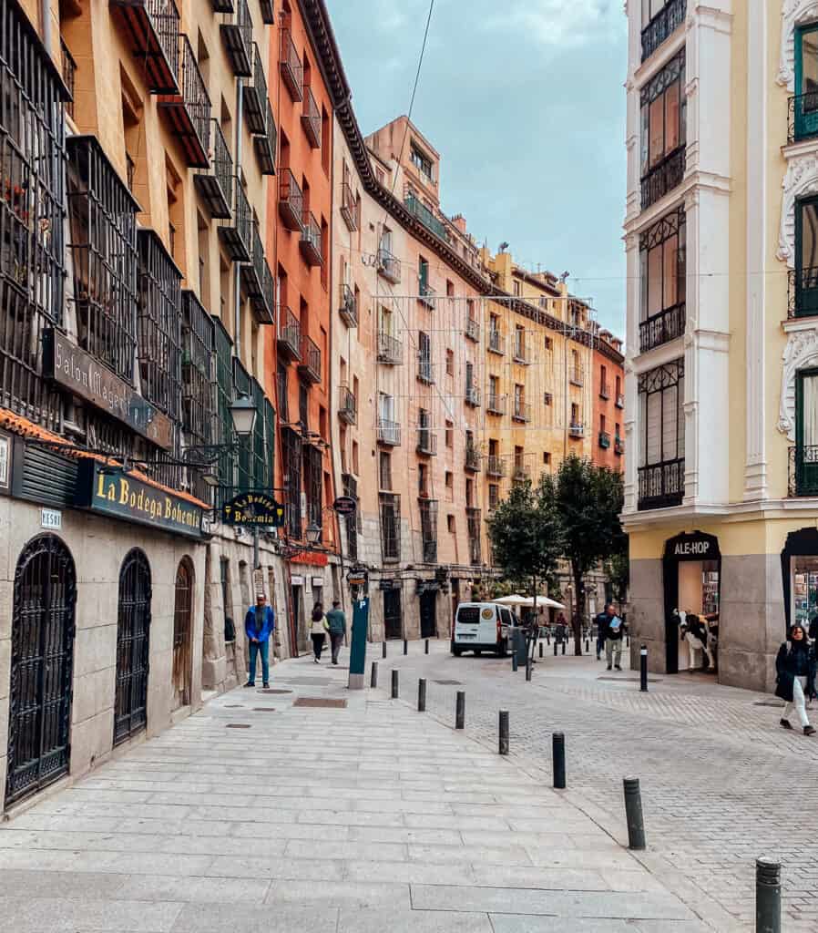 A bustling street corner in Madrid with diverse architecture, from traditional to modern, with people walking by shops and colorful facades, showcasing the vibrant city life.