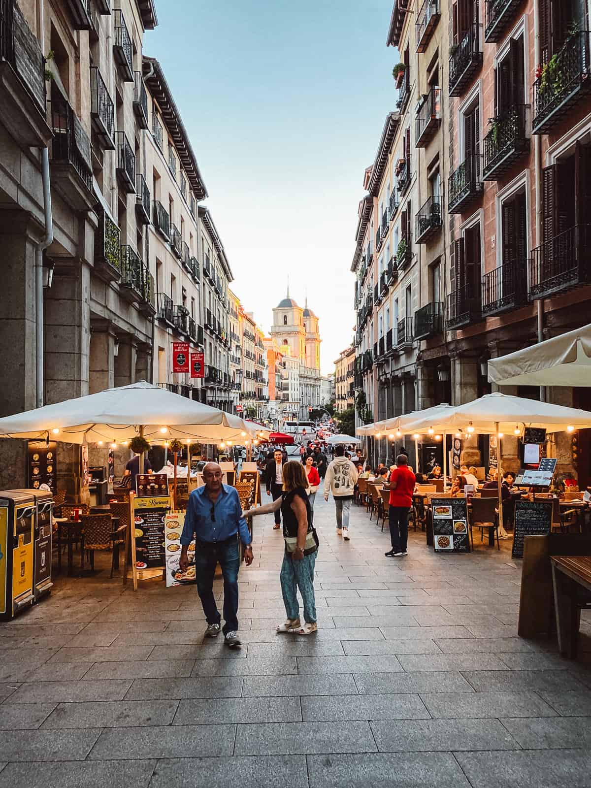 a street market in a pedestrian area in Madrid with vendors in tents with people walking
