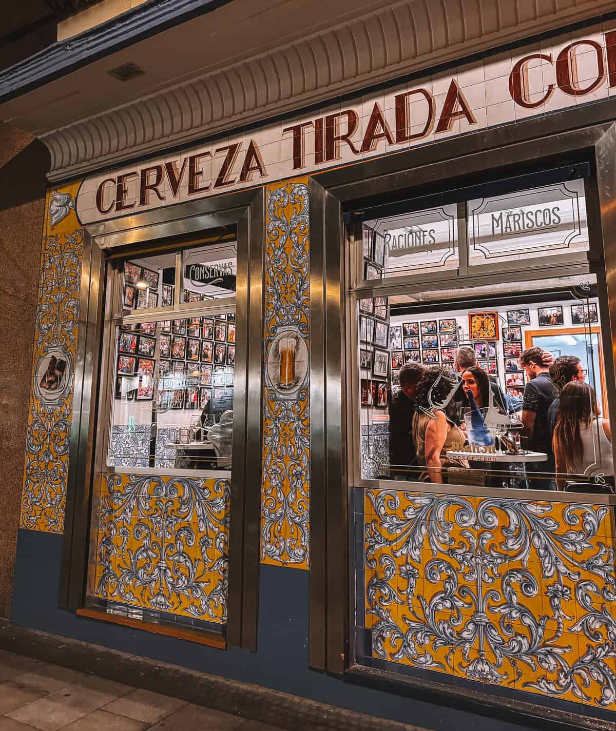 People eating inside a small tapas bar with yellow and blue ceramic tiled walls 