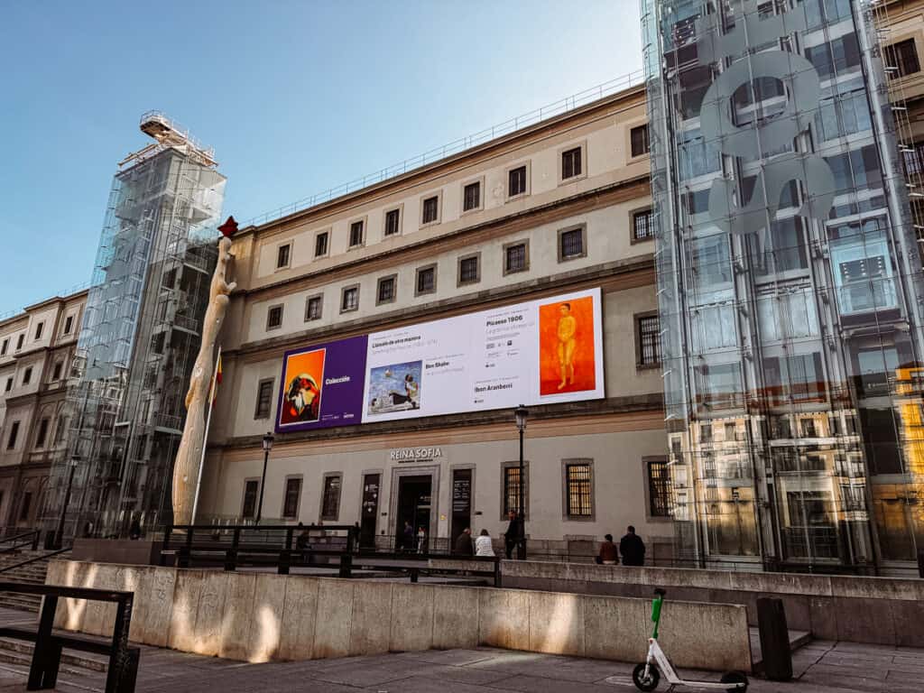 The Reina Sofia Museum in Madrid under clear blue skies, with banners displaying current exhibitions, reflecting the city's rich cultural scene and modern art focus.