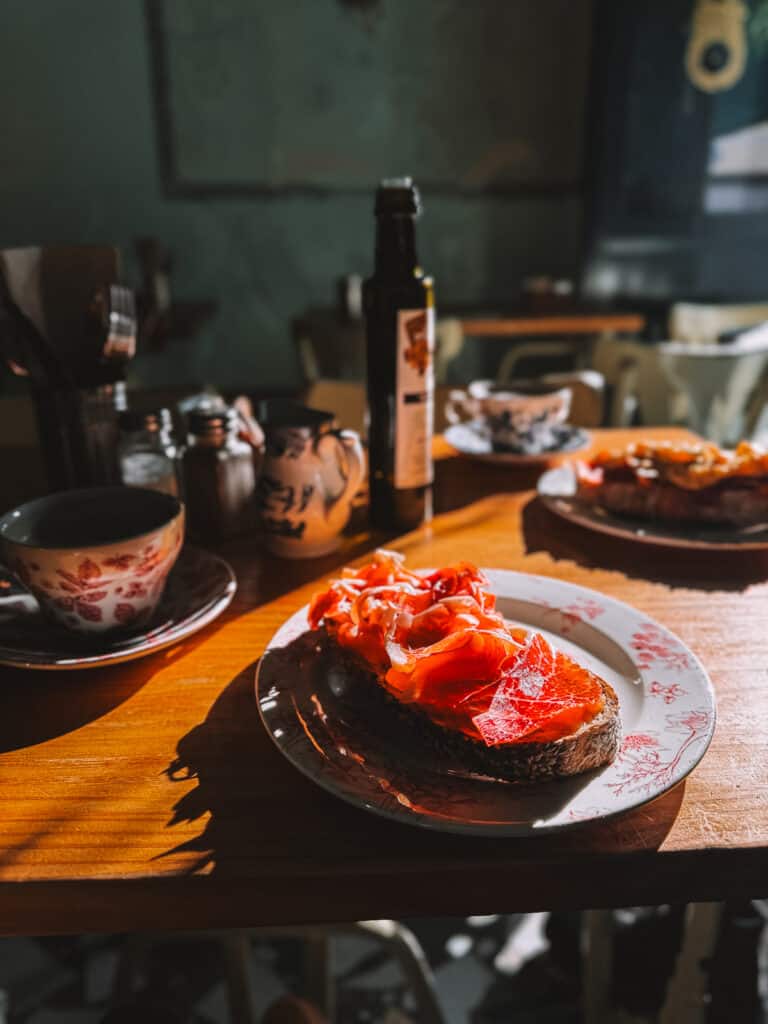 A rustic table setting featuring a slice of crusty bread topped with vibrant red tomatoes, accompanied by a coffee, basking in the warm glow of a Madrid café.