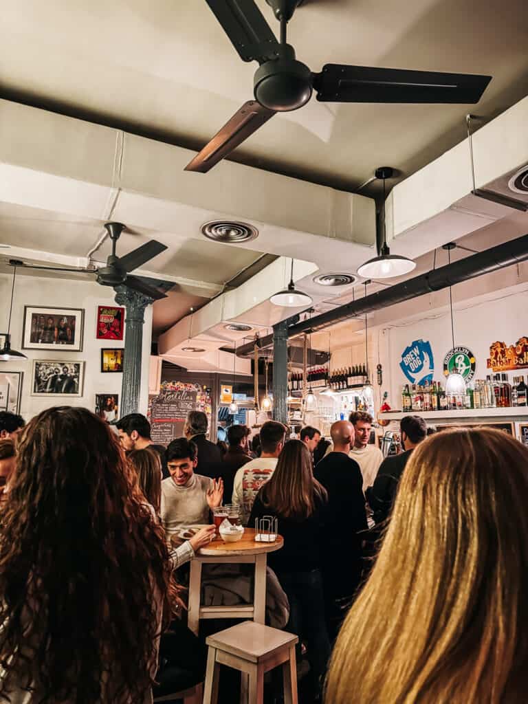 A lively bar scene captured from a patron's perspective, showcasing a diverse crowd, hanging lights, and a vibrant atmosphere