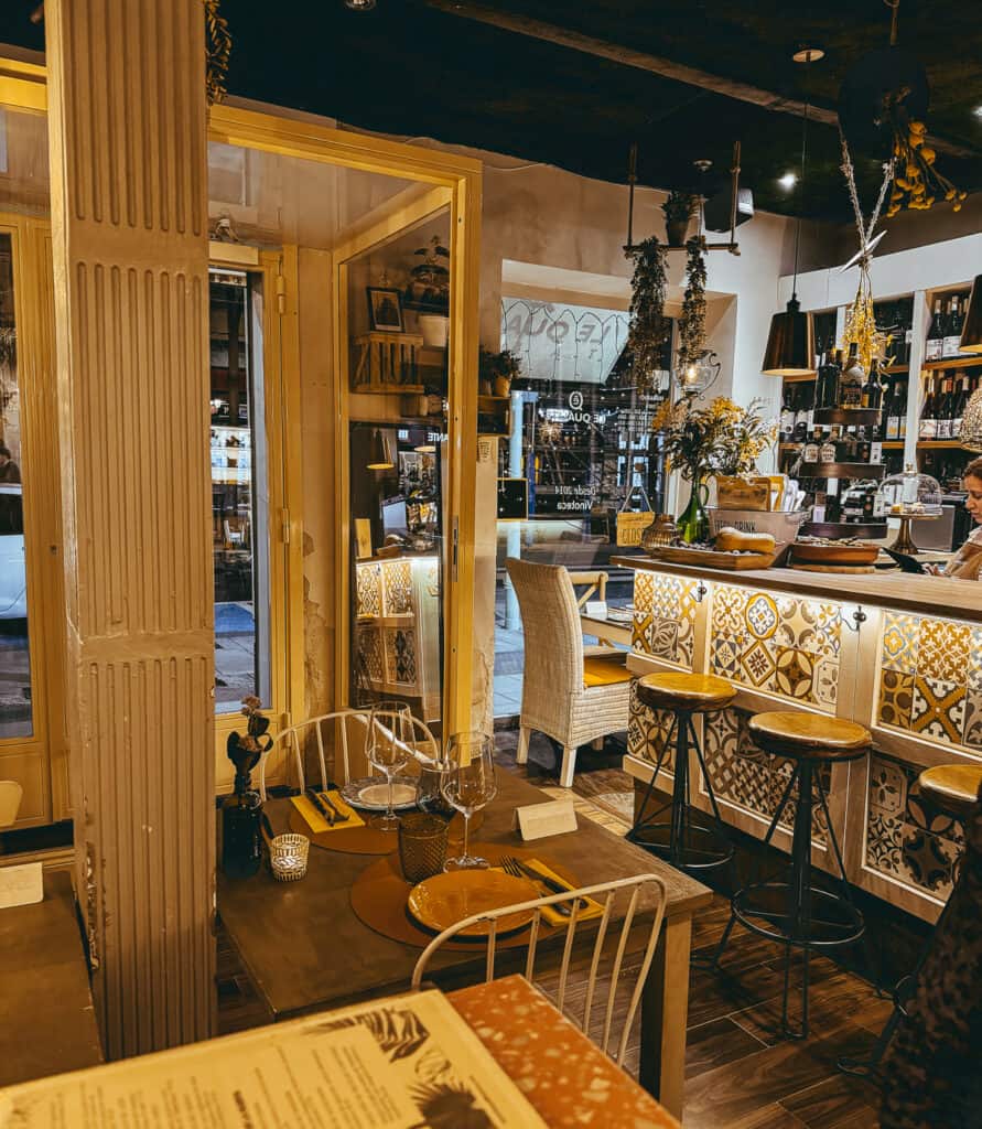 Cozy and inviting interior of a cafe with yellow walls, wooden and tile details, and plants hanging from the ceiling, providing a warm and homey dining environment