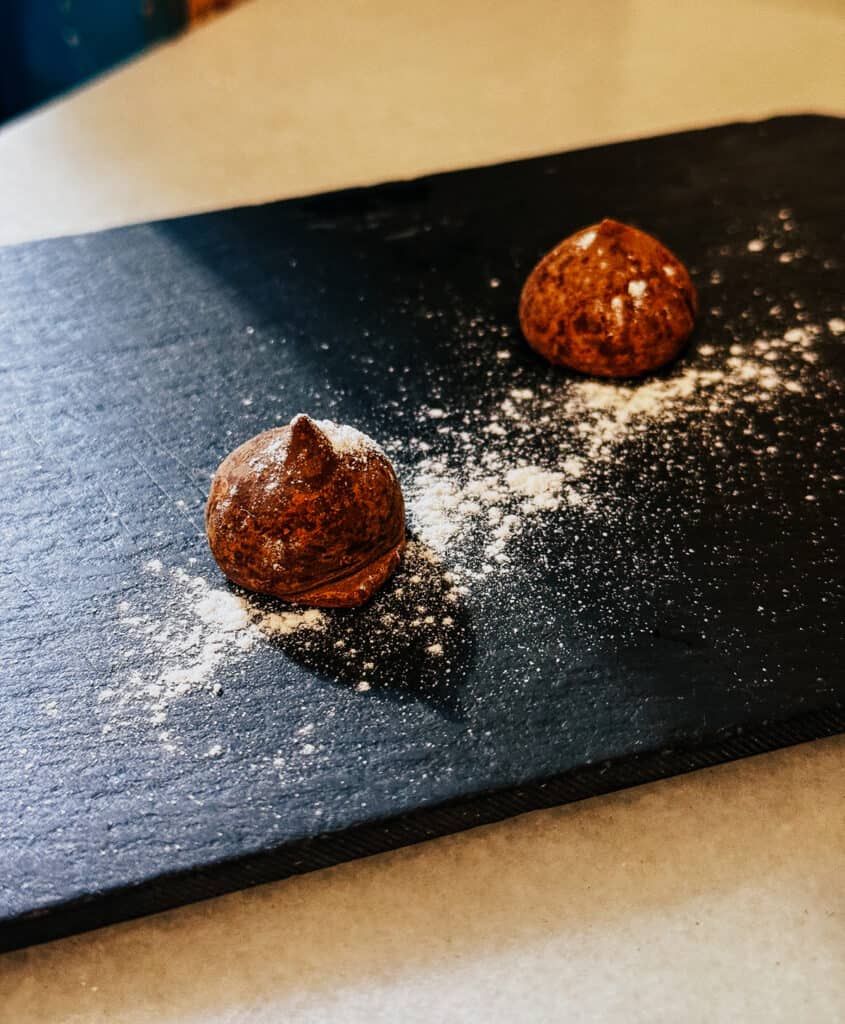 Two chocolate truffles dusted with powdered sugar on a dark slate, presenting a simple yet elegant dessert option