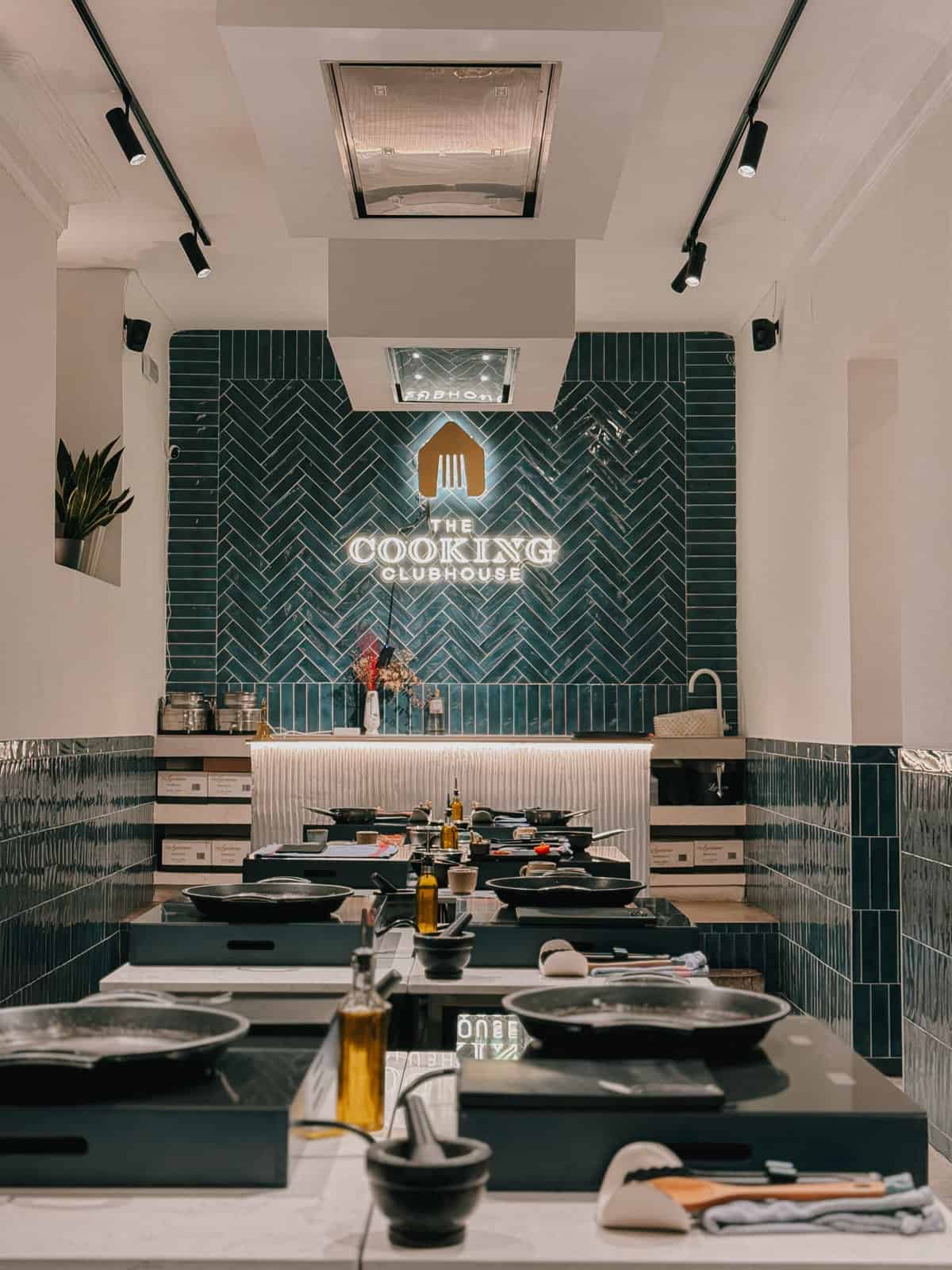 The elegant interior of The Cooking Clubhouse with a sleek, modern kitchen setup, featuring dark teal herringbone tiles and cooking stations ready for a culinary workshop, exuding a stylish and inviting atmosphere for food enthusiasts