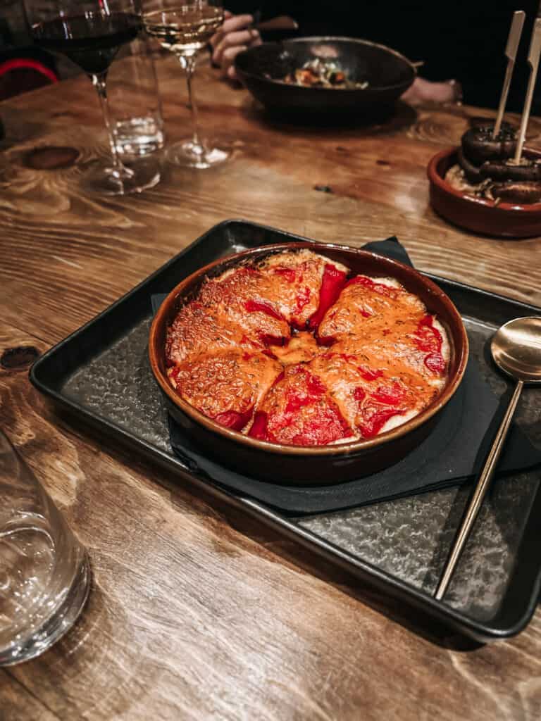 A delectable traditional Spanish dish served in a terracotta dish on a wooden table, surrounded by glasses of red and white wine, inviting diners to enjoy a flavorful culinary experience