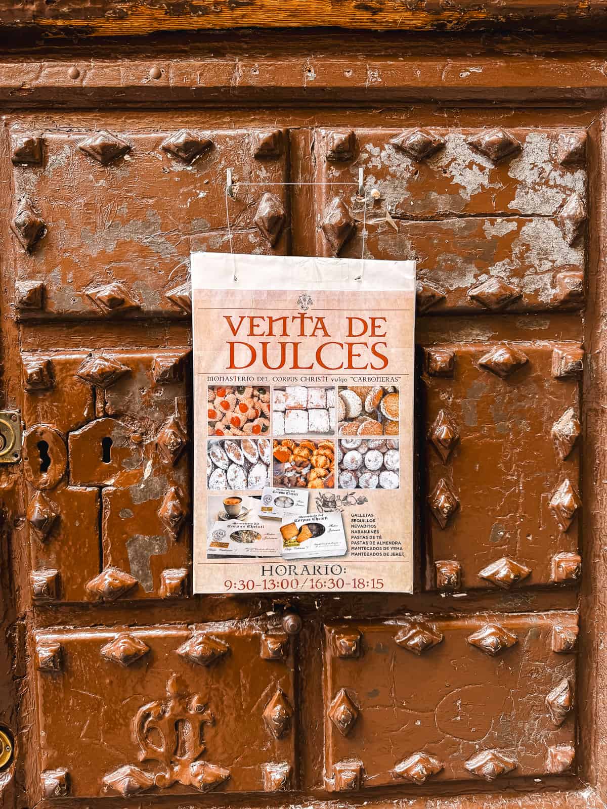 An aged wooden door displays a poster for 'Venta de Dulces' at the Monasterio del Corpus Christi, advertising traditional Spanish sweets with a schedule, evoking the historic charm of Madrid's convent confectioneries.