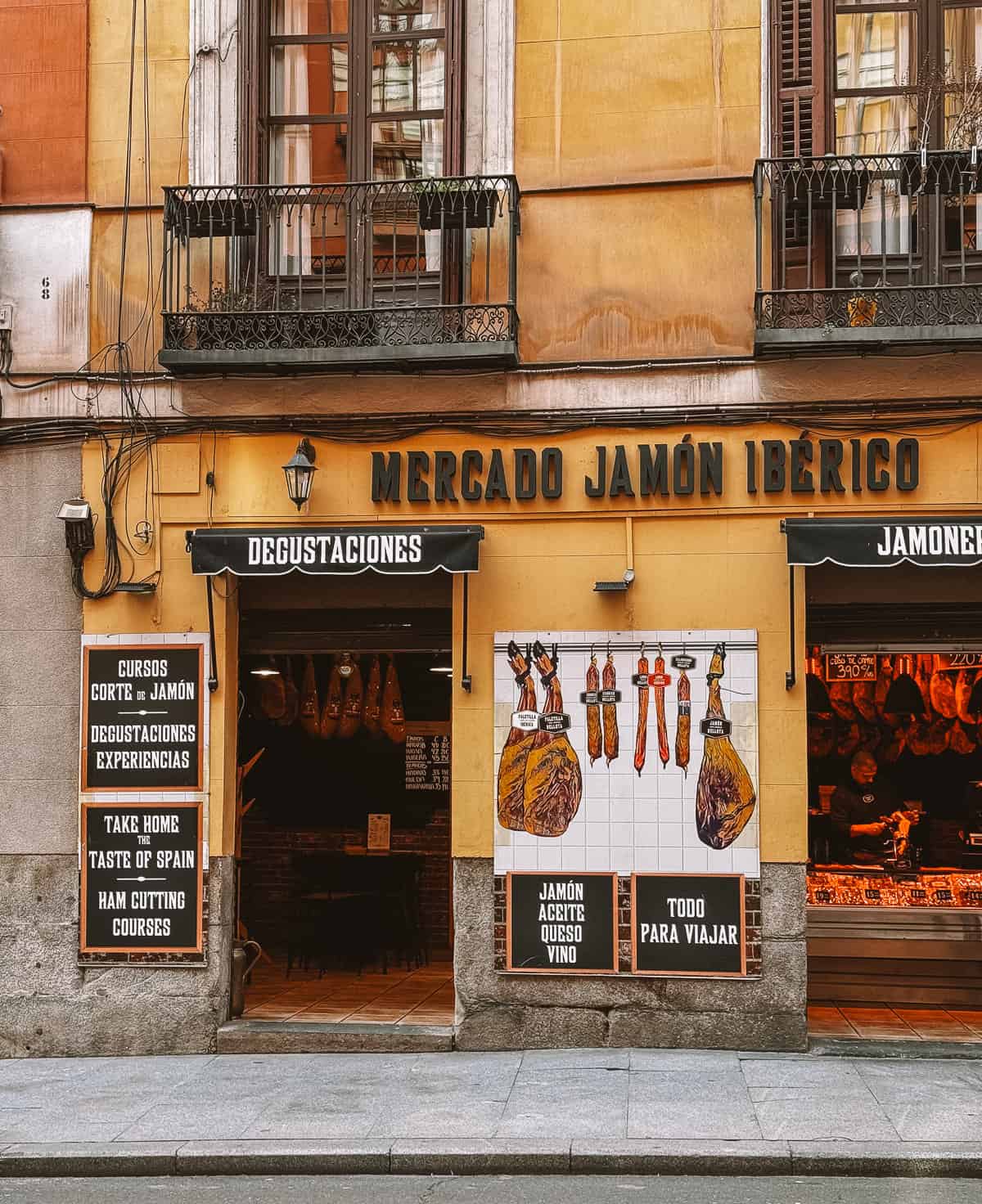 The storefront of Mercado Jamón Ibérico invites passersby with its bold signage, offering a taste of Spain through jamón, cheese, and wine, epitomizing the rich culinary culture of the region.