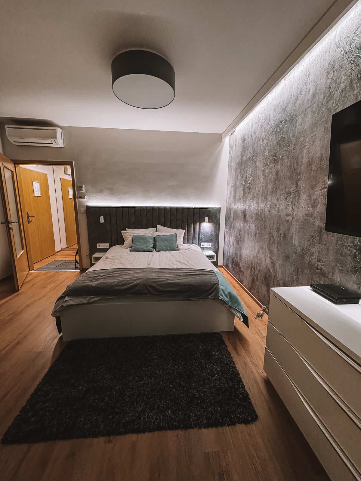 a modern hotel room with gray walls and a queen size bed with teal pillows