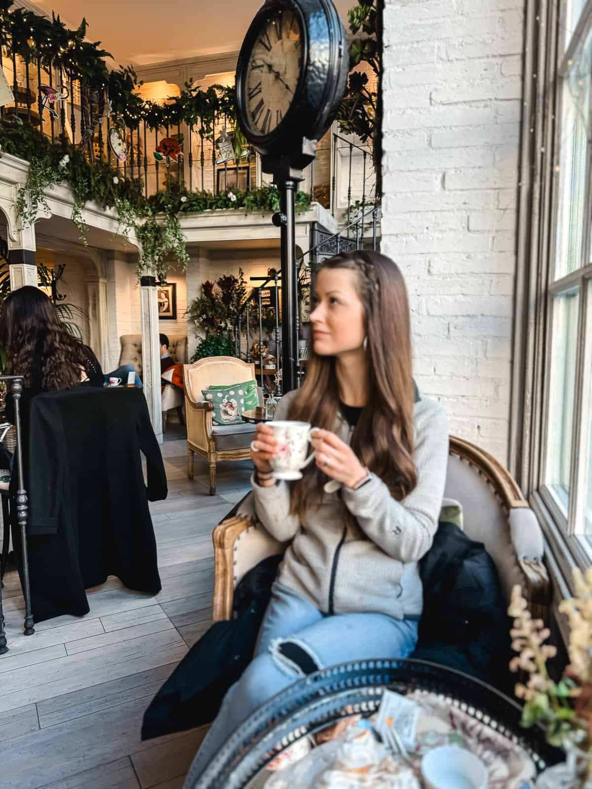 A woman enjoying a cozy tea time in a quaint café with a vintage interior and a lush green balcony in the background
