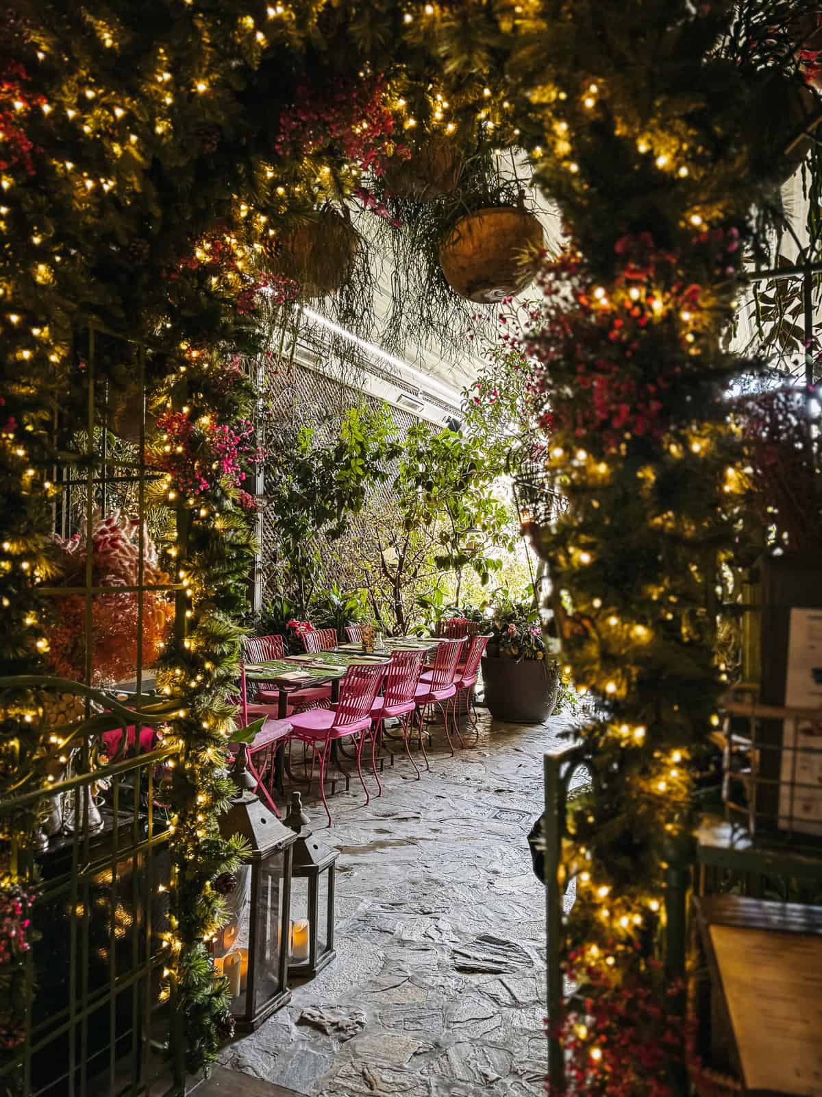 Fairy lights and blooming flowers decorate an enchanting courtyard of a secret garden restaurant, a hidden gem tucked away in Madrid.