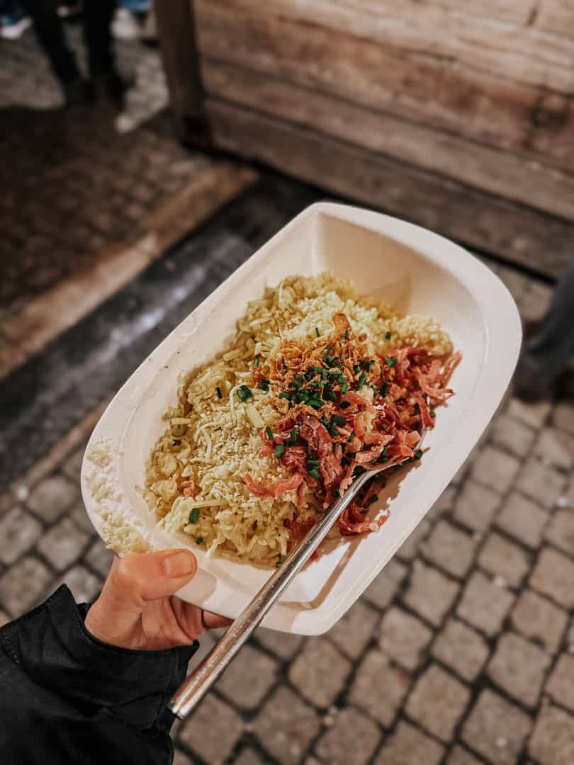 A person holding a plate of traditional German food, likely sauerkraut and crispy bacon, at a Christmas market in Berlin