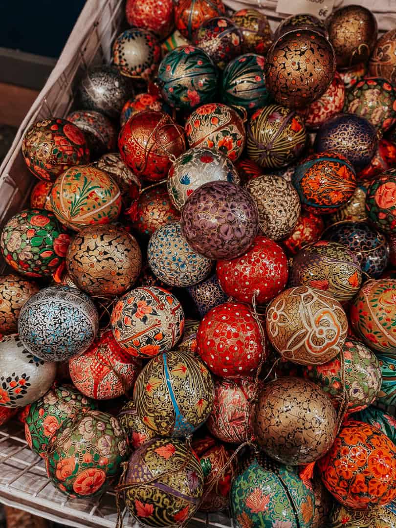 A close-up of a crate filled with ornately decorated Christmas baubles in a vibrant mix of colors and patterns, showcasing the intricate artistry of holiday ornaments.
