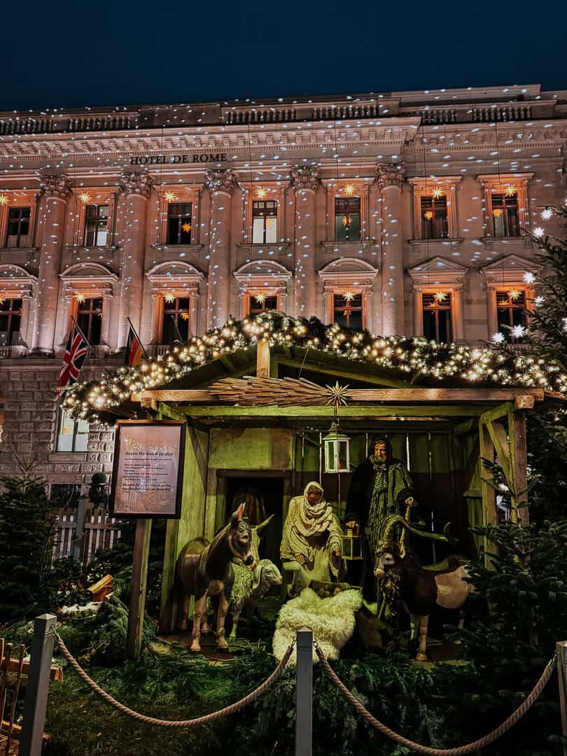 A nativity scene with life-sized figures in front of the Hotel de Rome in Berlin, adorned with Christmas lights and a starry sky.
