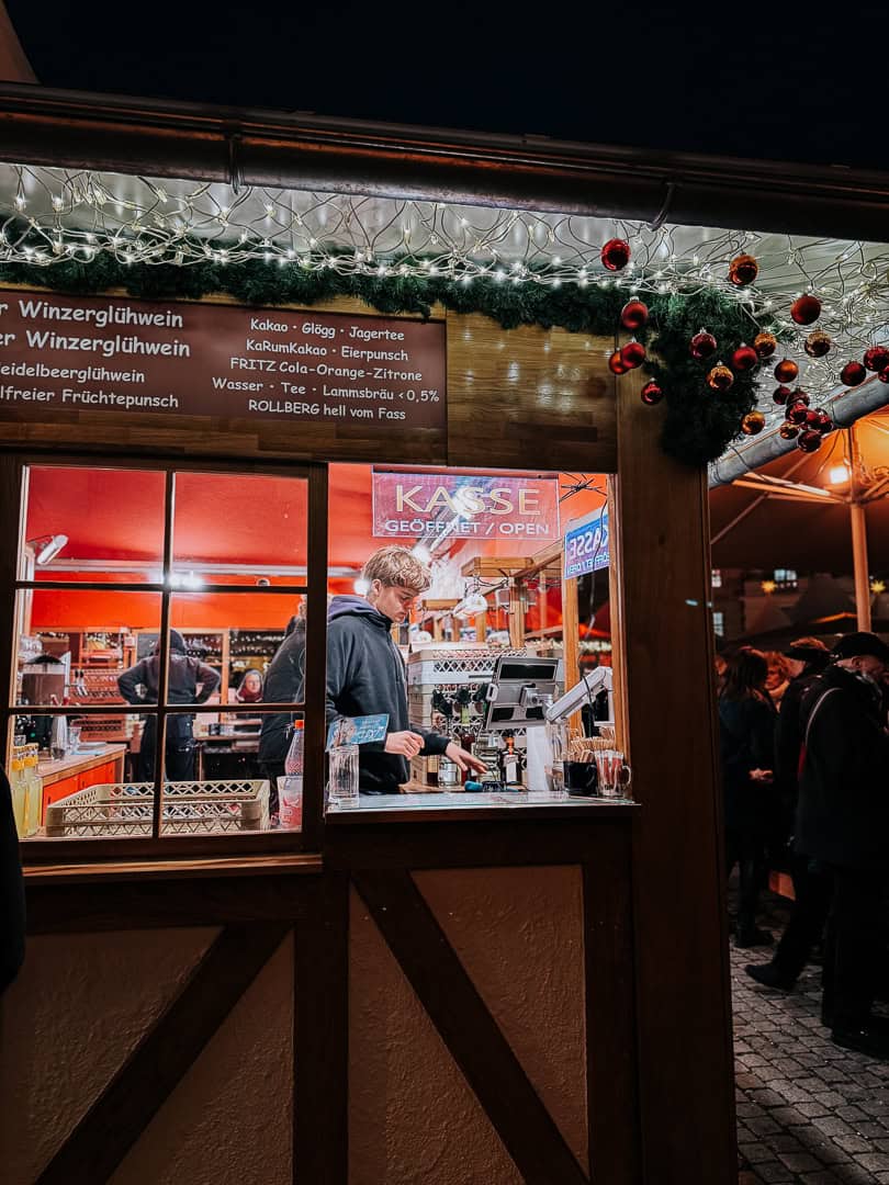 A close-up of a Christmas market stall window displaying a menu with drinks like cocoa and Glögg, and festive decorations in Berlin.