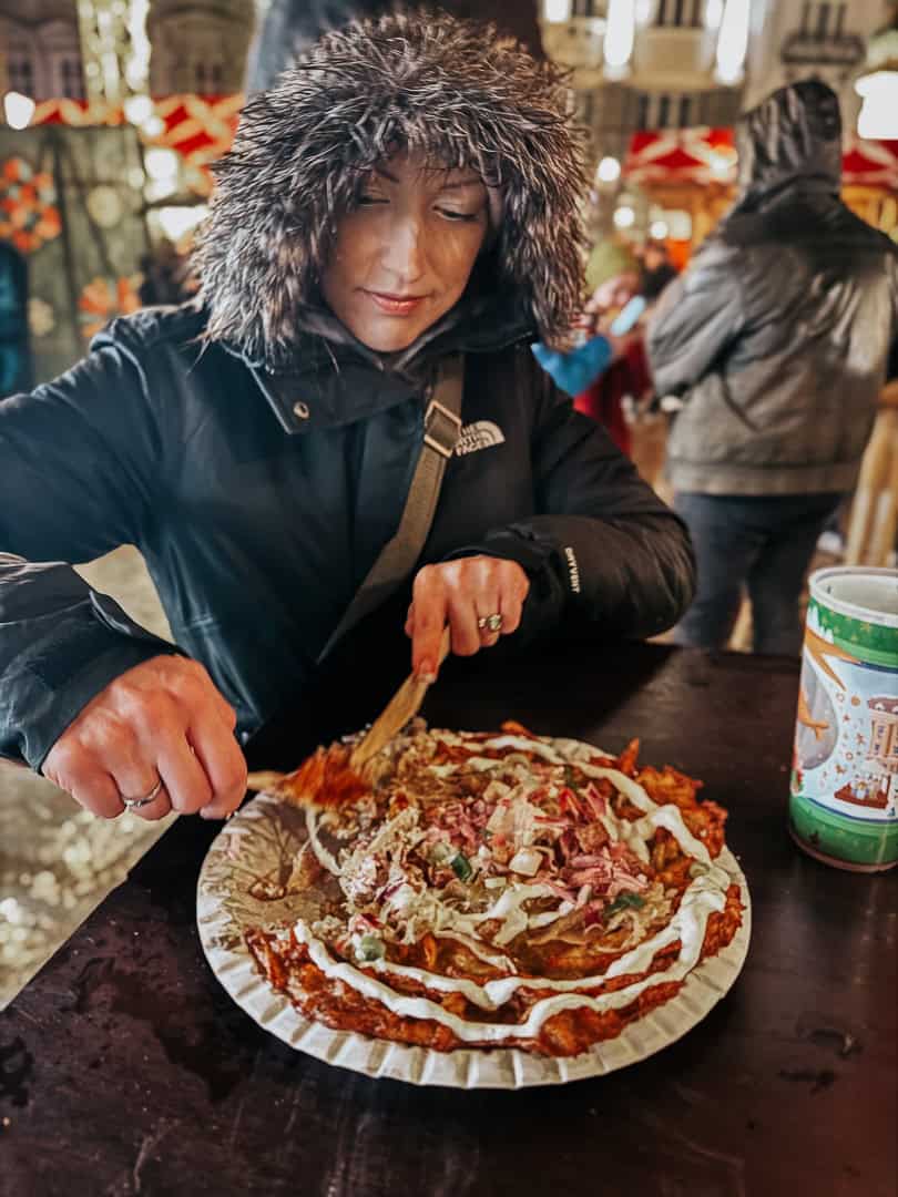 A woman in a fur coat eats a large potato pancake
