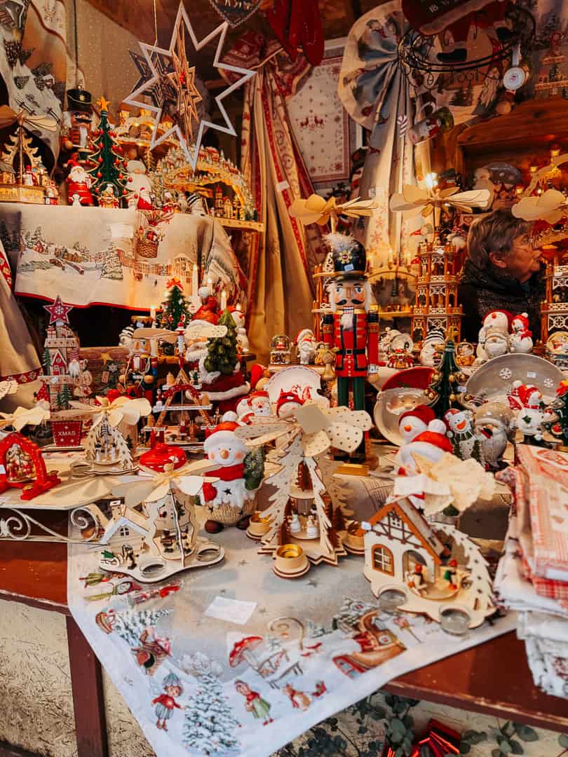 A variety of wooden Christmas decorations and toys, including nutcrackers and snowmen, are artfully displayed at a market stall, evoking a traditional festive spirit.