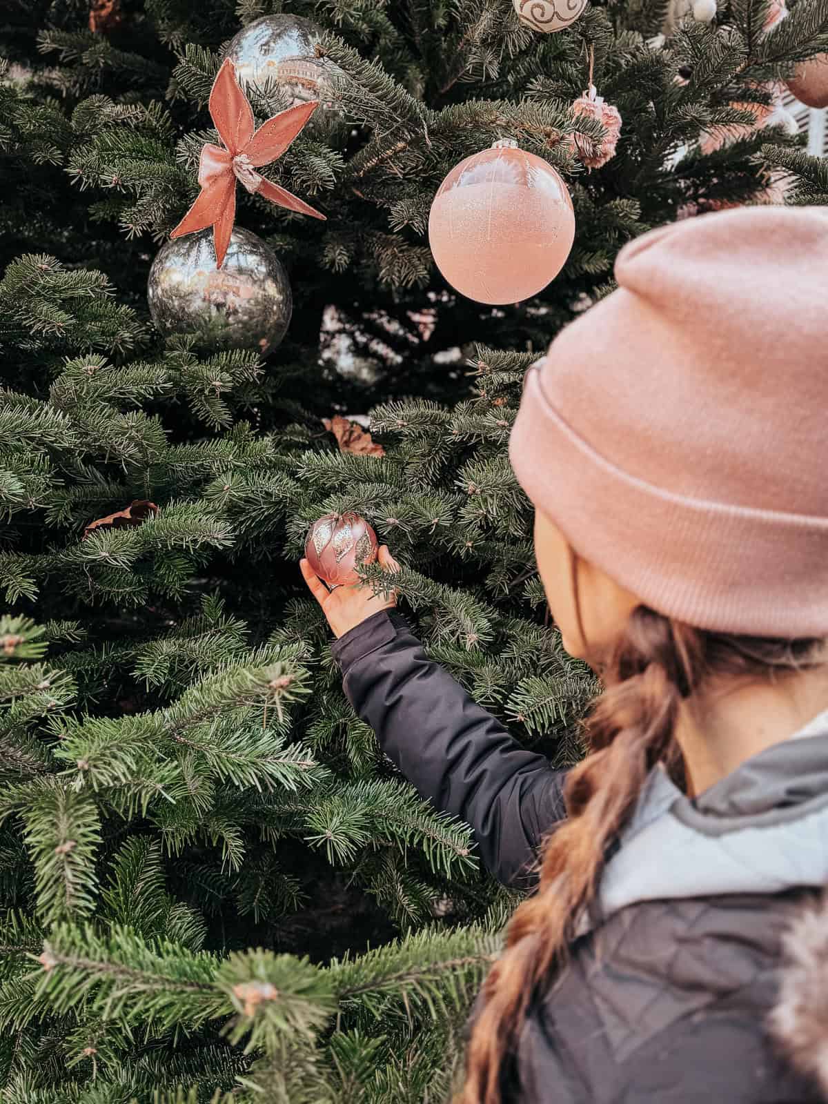 A child reaching out to a Christmas tree adorned with large baubles and bows, capturing the magic of festive decorations in Colmar.