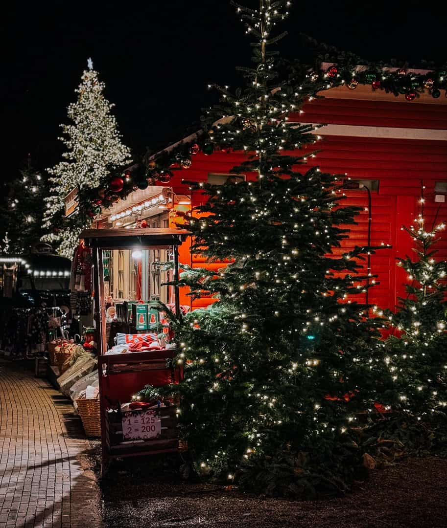 Twinkling Christmas trees flank a red market stall at night in Copenhagen, with holiday decorations and goods on display for sale