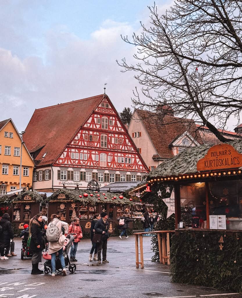 Traditional German half-timbered house adorned with Christmas decorations overlooking a bustling Christmas market stall selling Hungarian chimney cakes