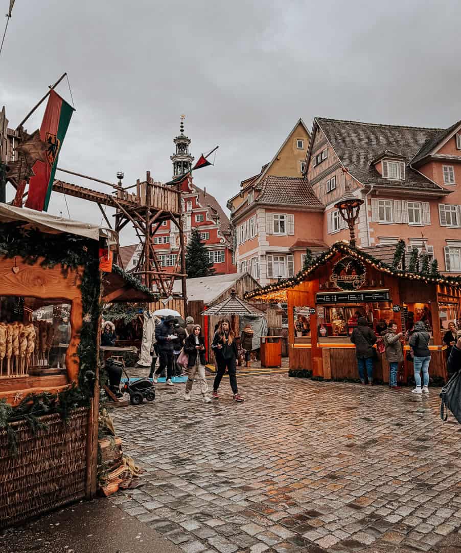 Visitors meander through the Esslingen Christmas market, with cobblestone streets leading to warmly lit, festive stalls and a historic town hall tower in the background