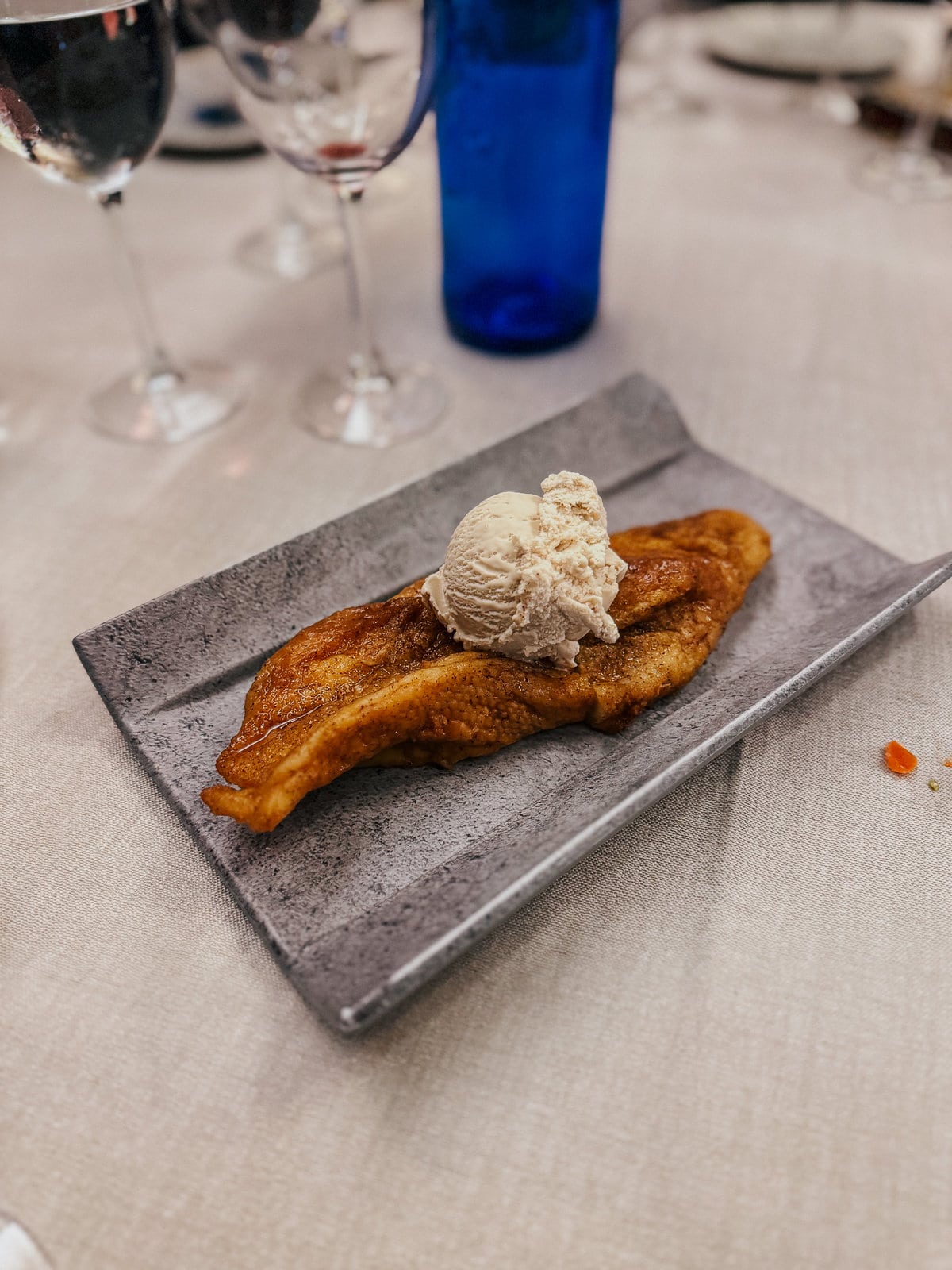 golden brown Spanish french toast with a scoop of ice cream on a white table with a blue glass of water
