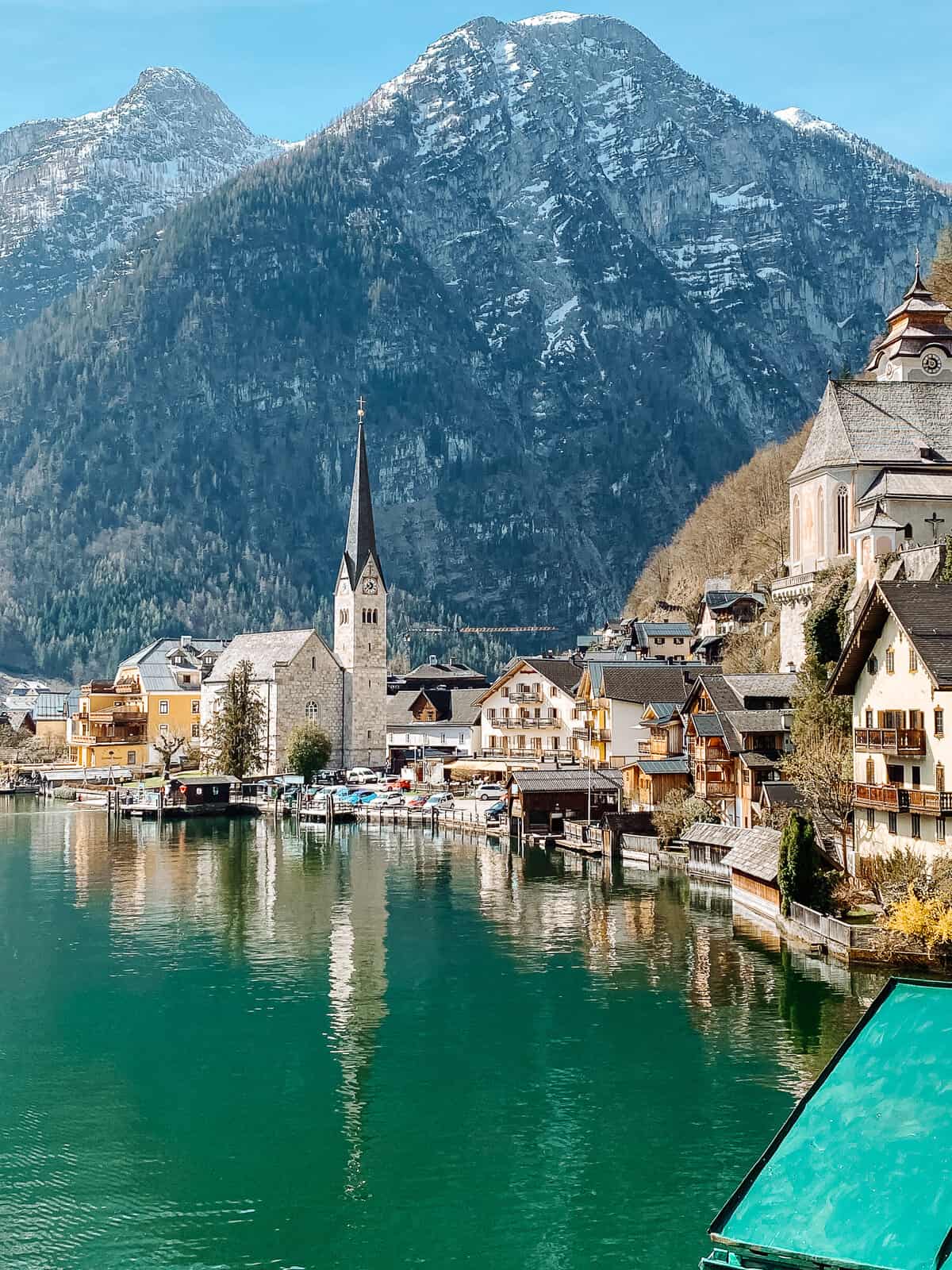 The picturesque village of Hallstatt in Austria, with its beautiful church spire and traditional buildings set against the stunning backdrop of alpine mountains and the reflective waters of Hallstatt Lake.