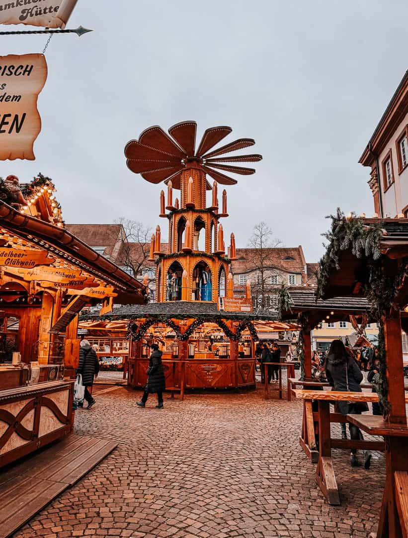 A unique wooden Christmas pyramid decoration towering over a market, with intricate details and warm lighting, set against a cloudy sky with market activity below.