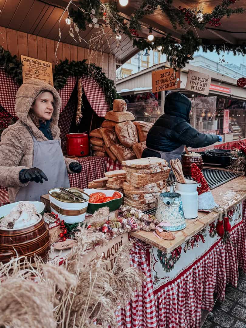 A Christmas market stall with a vendor selling traditional Polish bread and a sign reading 'Old Polish Style Slice of Bread' in Krakow
