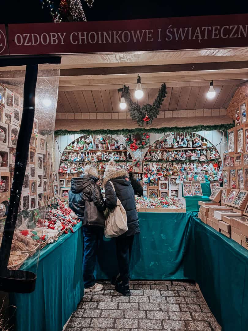 Shoppers browsing a Christmas market stall with a variety of festive ornaments and gingerbread in Krakow, Poland.