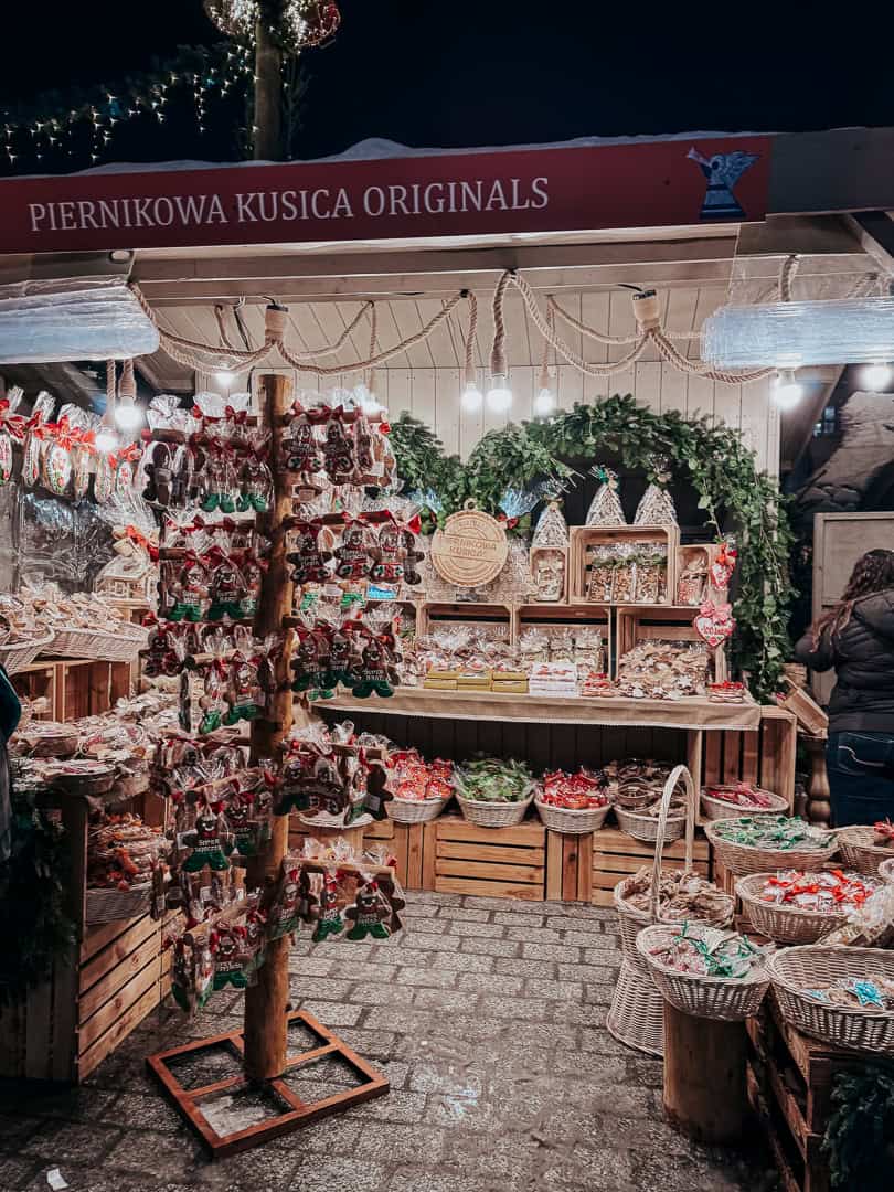 Elaborate Christmas market stall selling gingerbread cookies and confectioneries, with a 'Piernikowa Kusica Originals' sign in Krakow