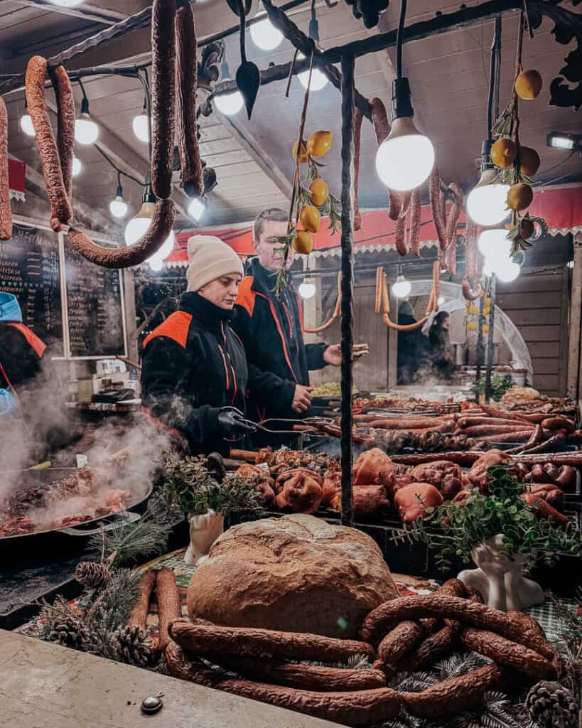 Delicatessen stall with an assortment of smoked sausages and meats, with vendors serving in a festive market setting in Krakow.